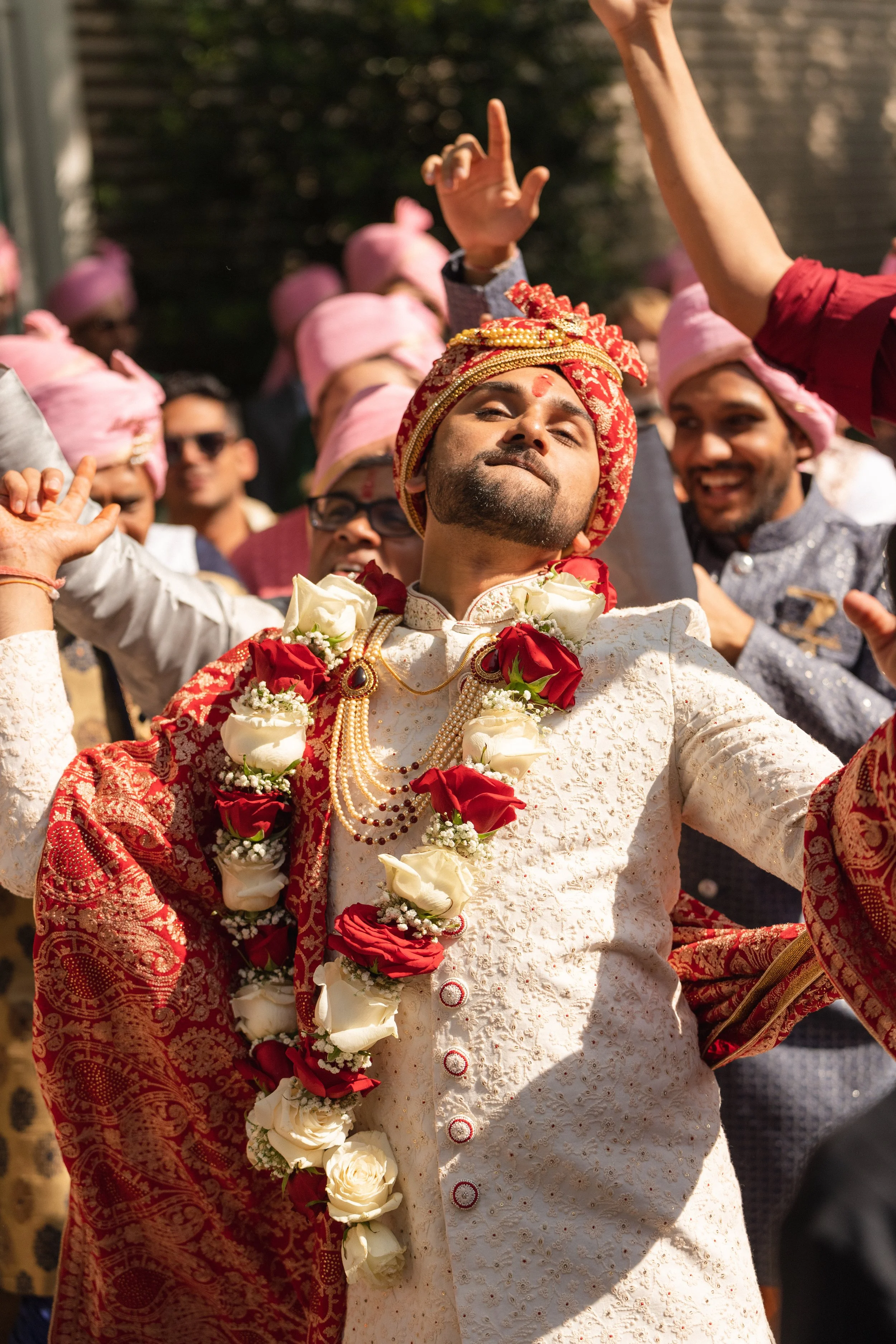 Groom in ornate sherwani and red turban surrounded by friends and family, captured in cinematic detail by Caz Isaiah — India Wedding Photographer