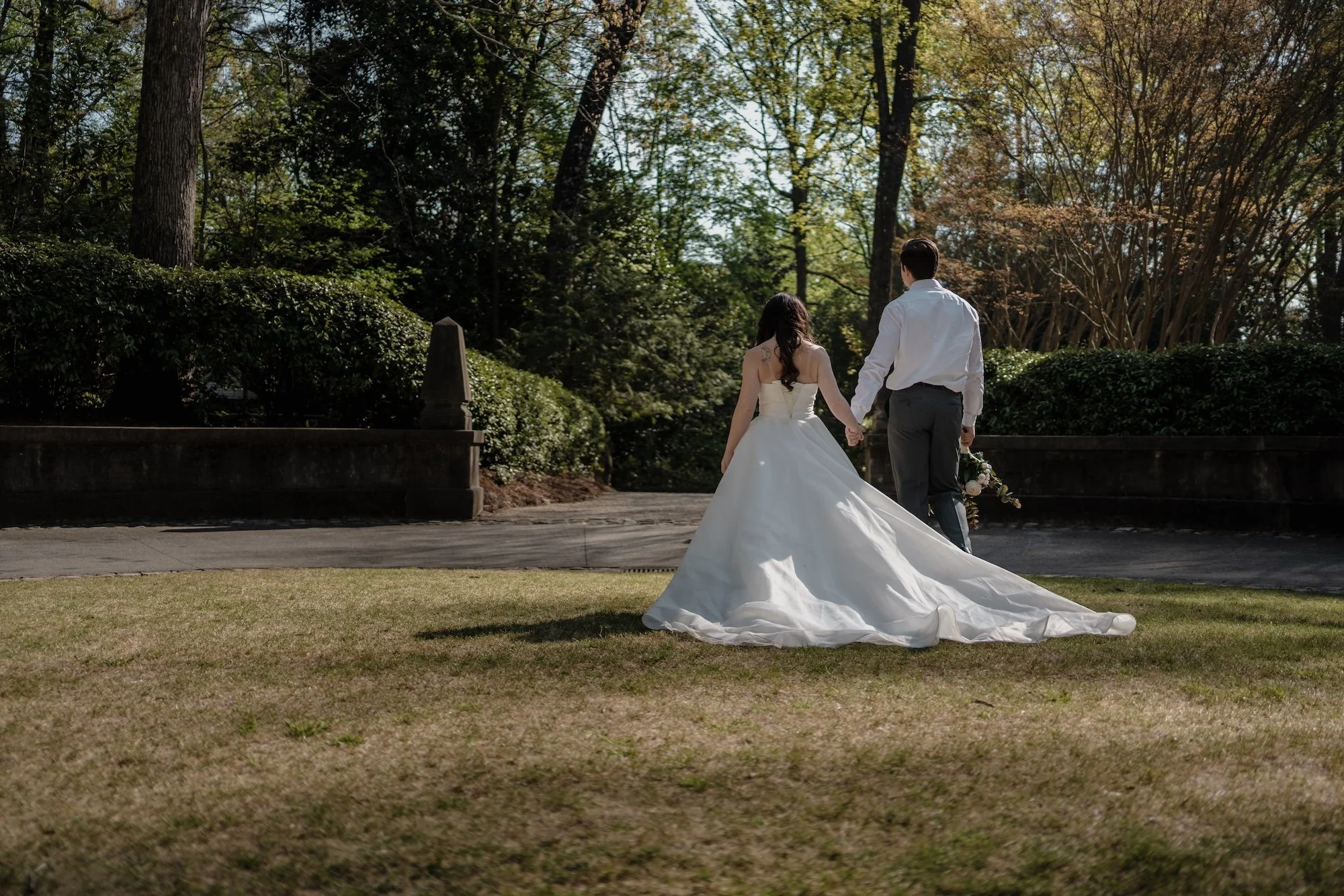 A bride and groom walk across an open garden, the gown trailing behind in elegant movement.