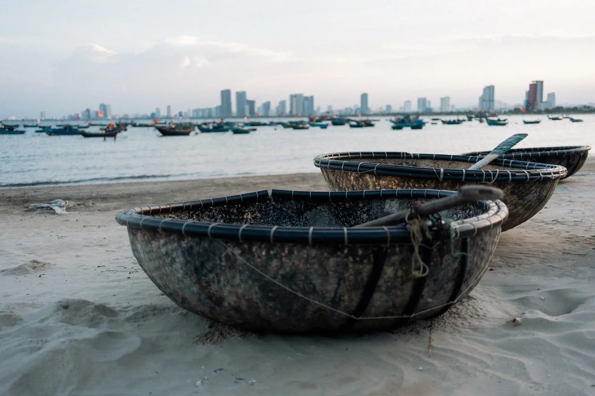 A round fishing boat resting on sand with a skyline in the distance, coastal wedding photography atmosphere in Da Nang Vietnam