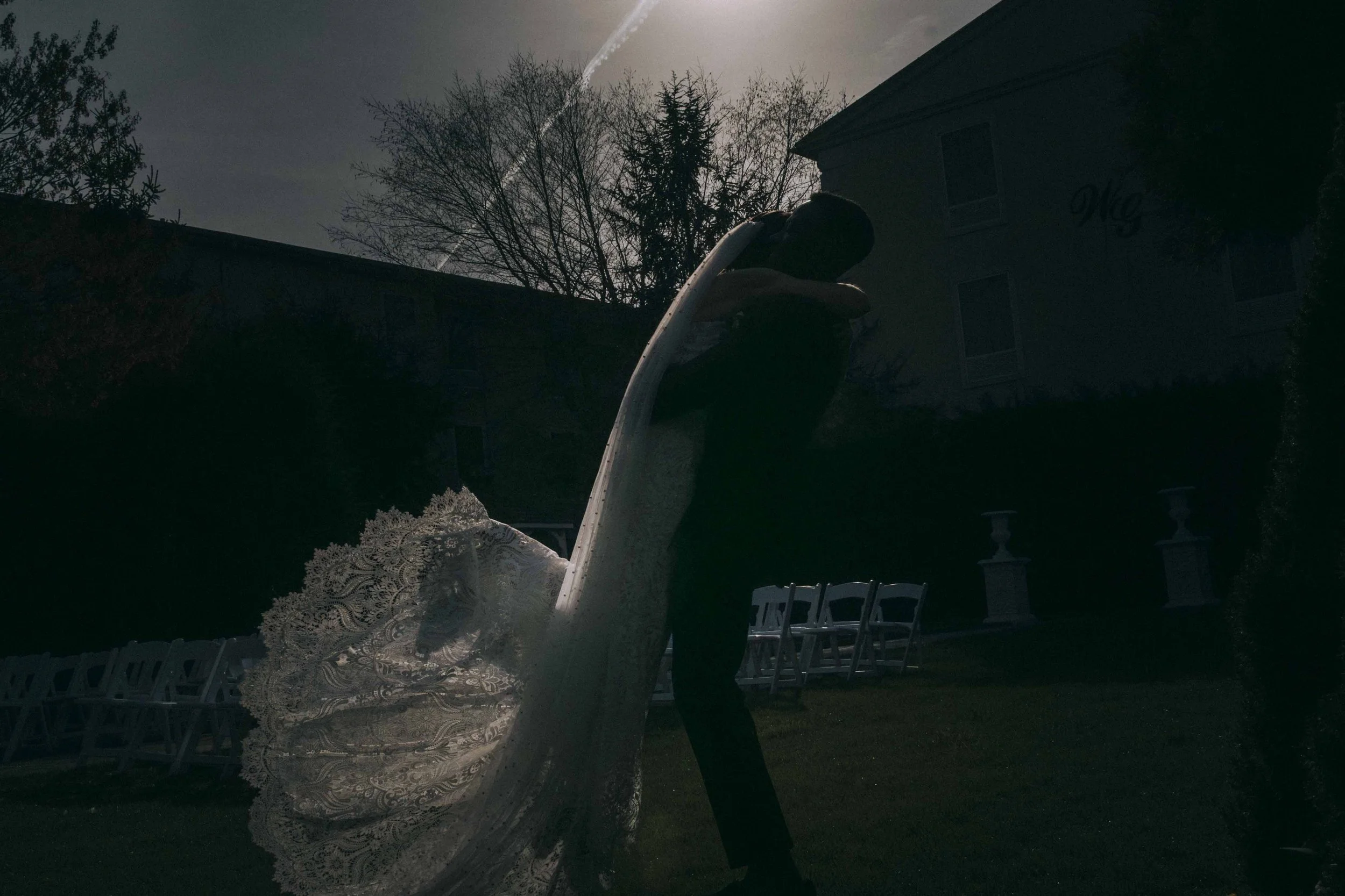 Groom lifts his bride beneath twilight sky, her veil illuminated by fading light — inspired by Habitas AlUla’s quiet romance and desert atmosphere.
