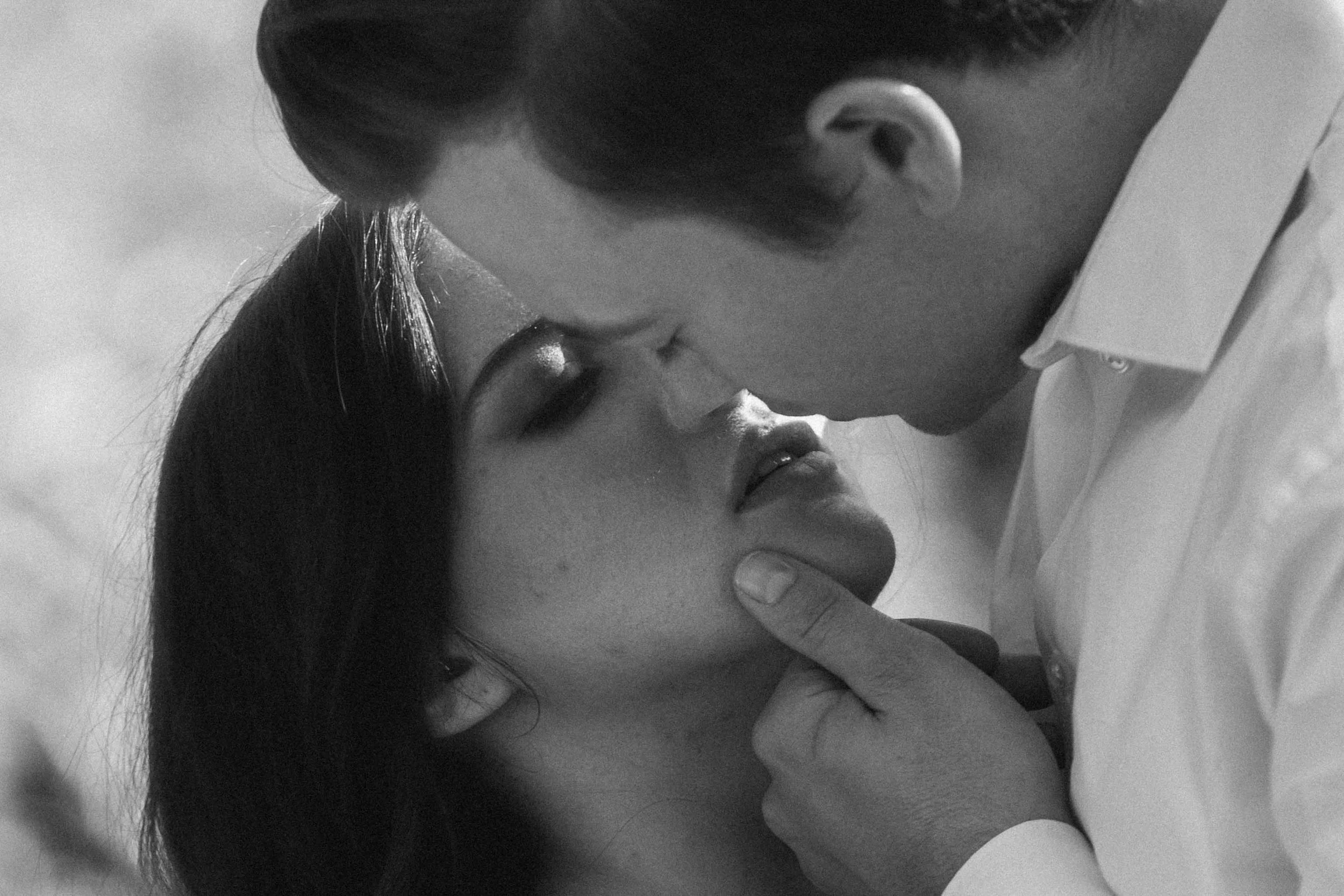 A couple leans toward each other while one gently lifts the other’s chin, framed tightly in intimate monochrome by a Fragmented Memories couples photographer.