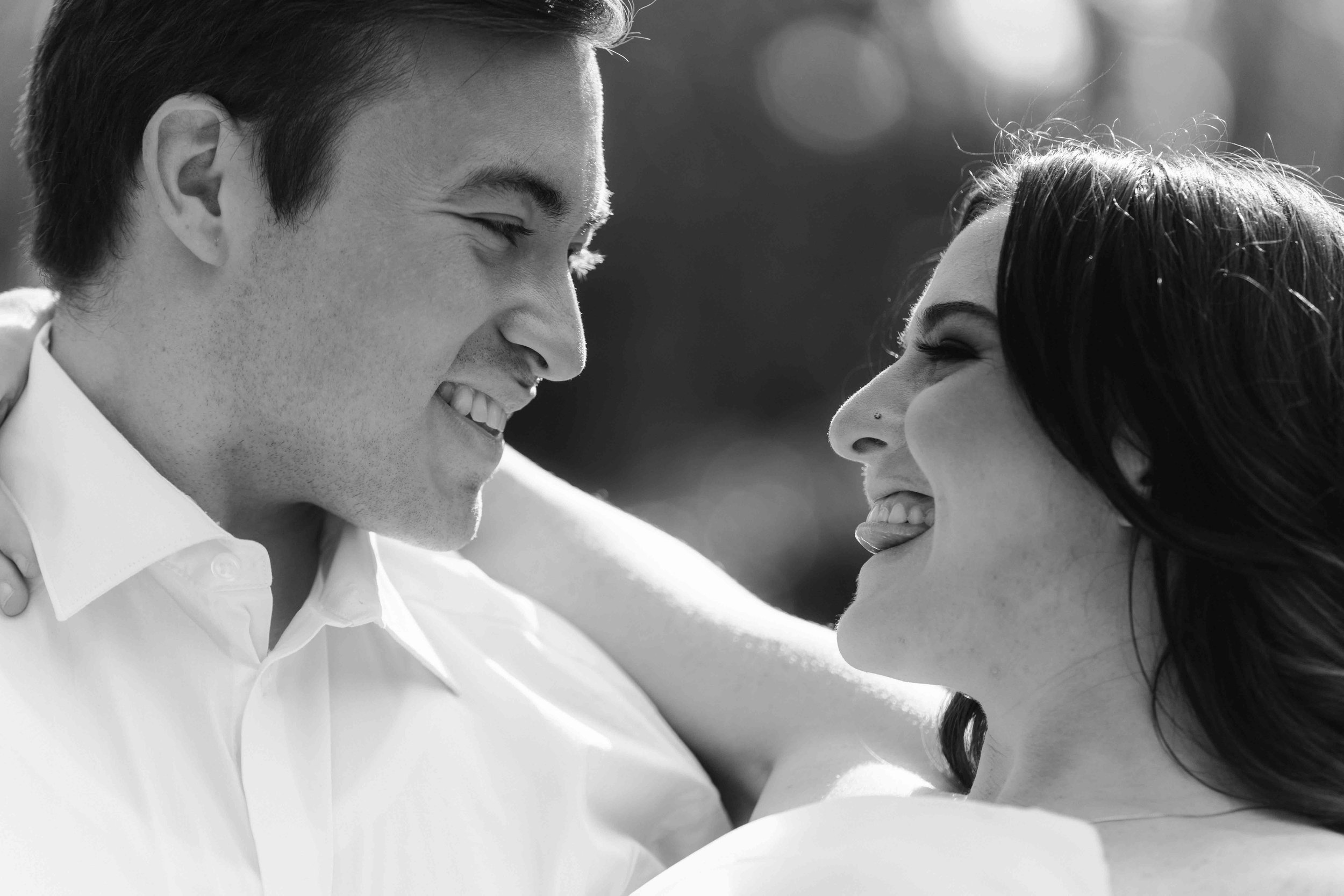 A couple smiles closely face to face, arms resting across shoulders, captured softly in black and white without a visible keyword.
