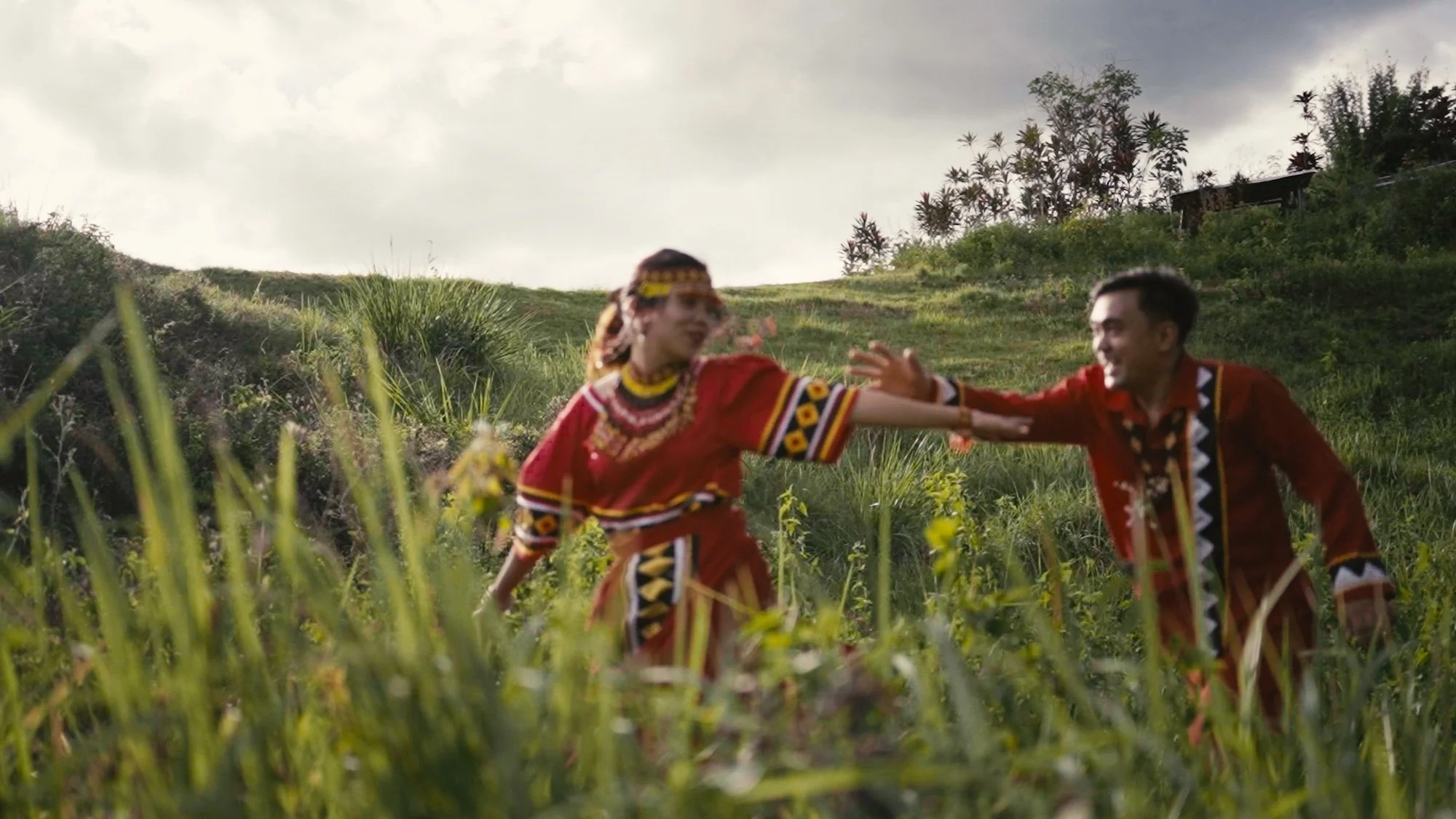 Couple in traditional attire runs through tall grass, hands reaching toward each other, captured by Scotland Wedding Photographer Caz Isaiah
