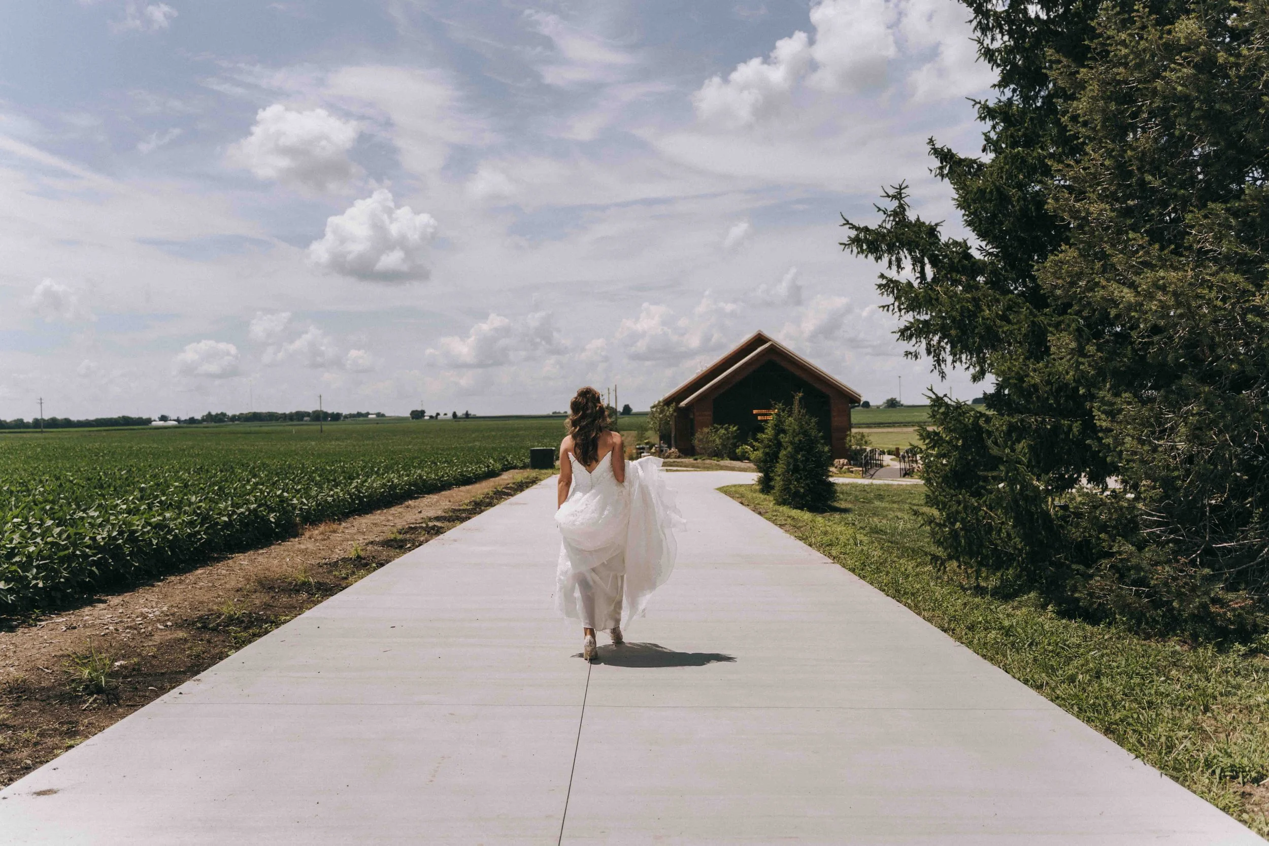 Bride walks a sunlit path toward her ceremony, framed by open skies and tropical stillness.