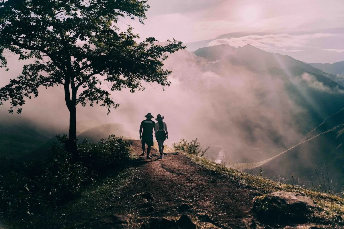 A couple walking along a ridge at sunrise, mountains fading into pink mist behind them