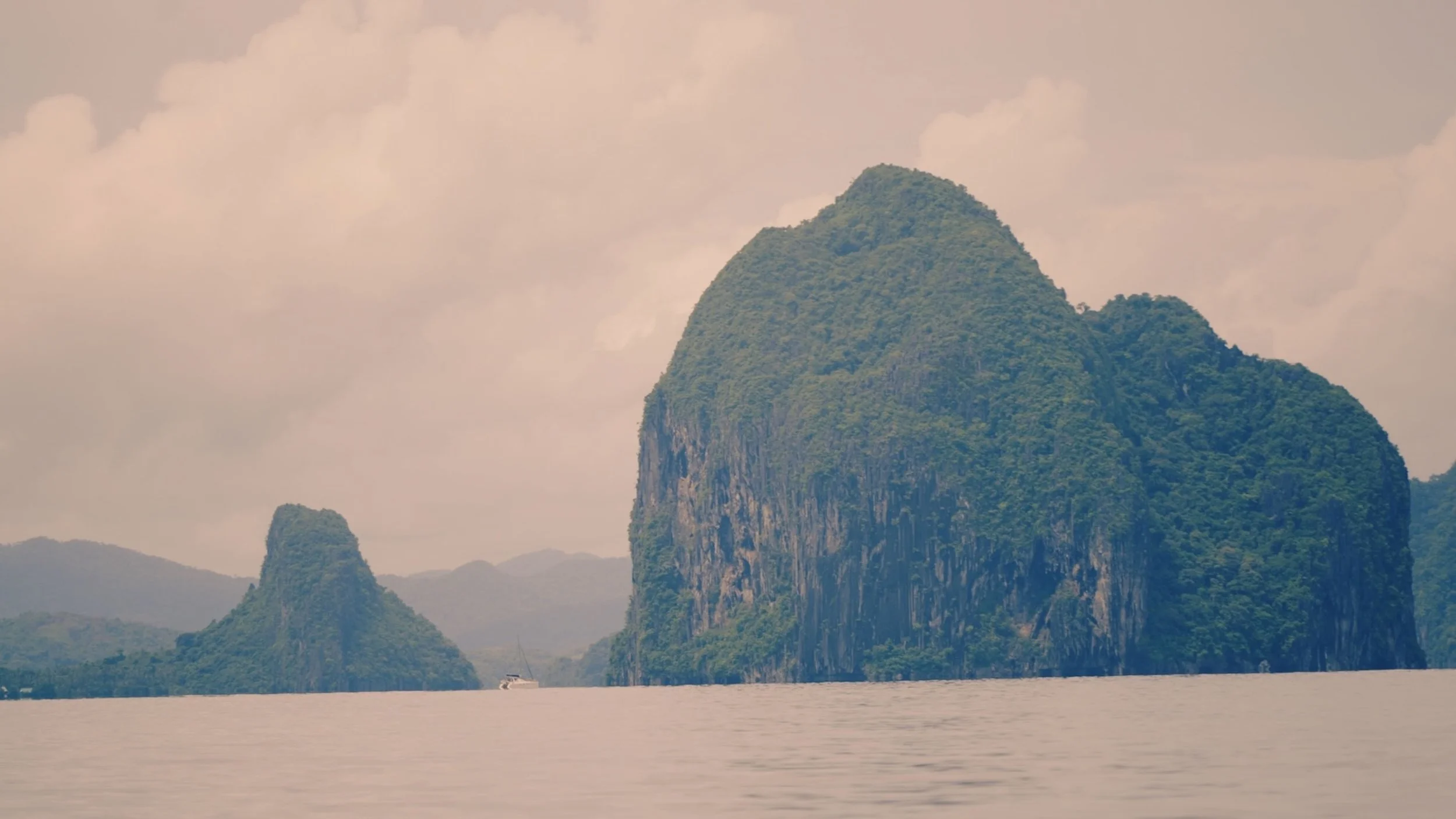 Two limestone formations rise from calm water as a small boat passes below, captured wide by a Fragmented Memories prenup photographer.