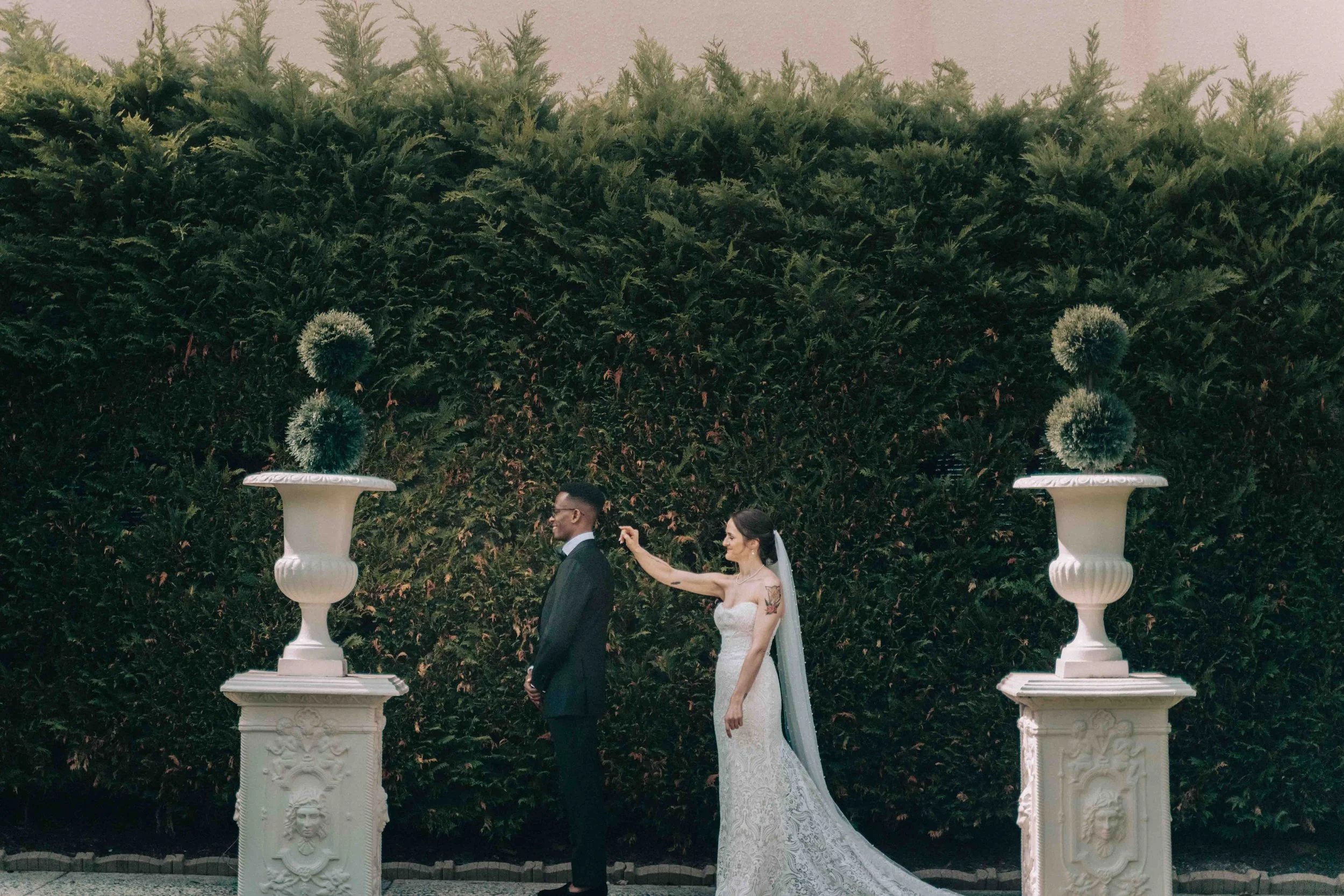 couple standing between marble urns in a serene garden, photographed by Caz Isaiah inspired by St Moritz