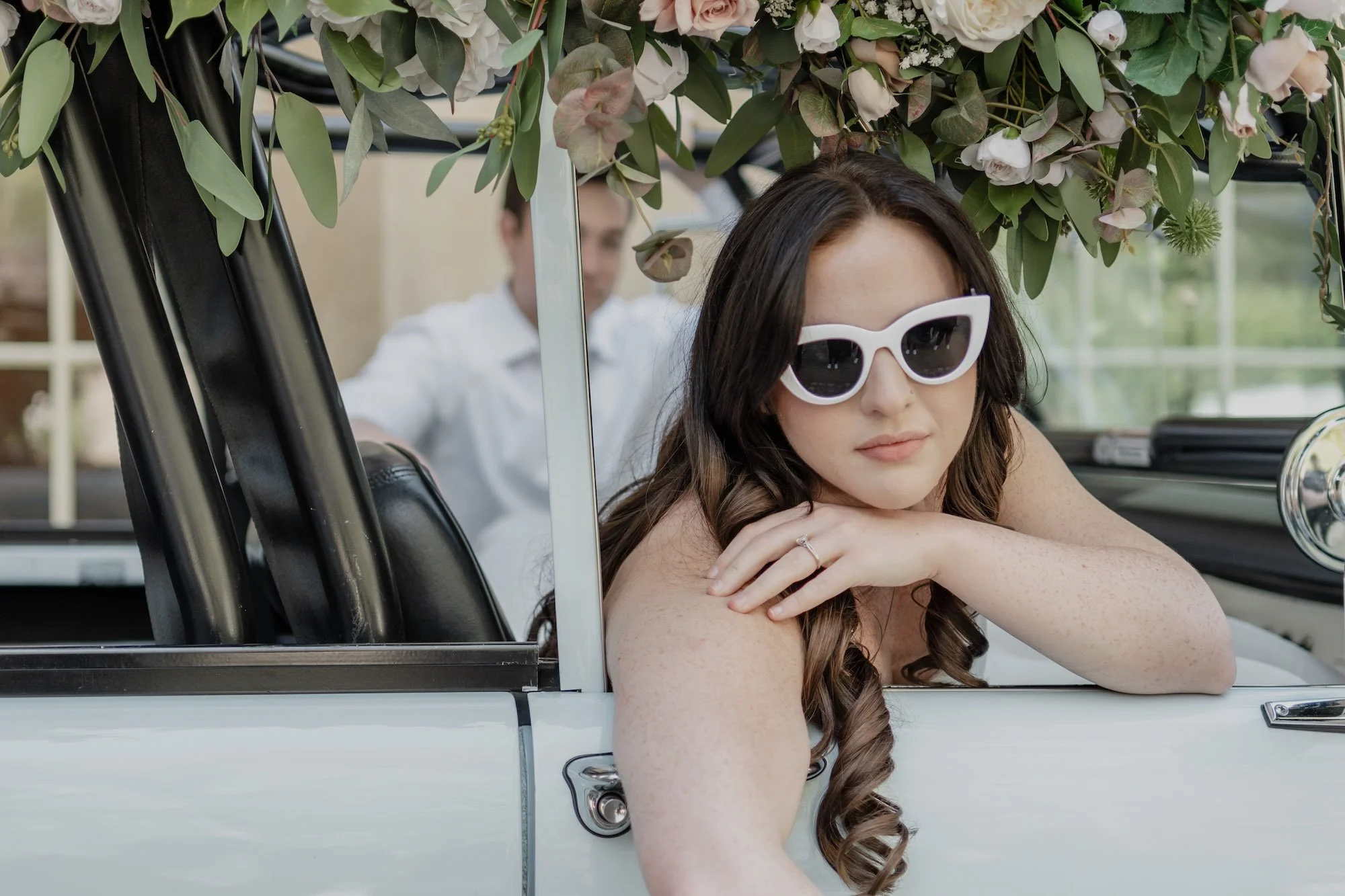 Bride in white sunglasses rests her arm on a vintage car door, cinematic detail captured in Los Angeles wedding photography