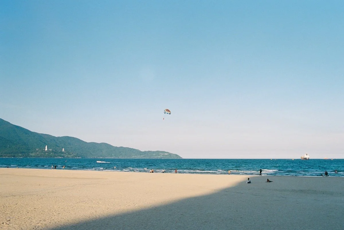a Nang proposal photographer – My Khe Beach shoreline with parasailing and mountains in the background
