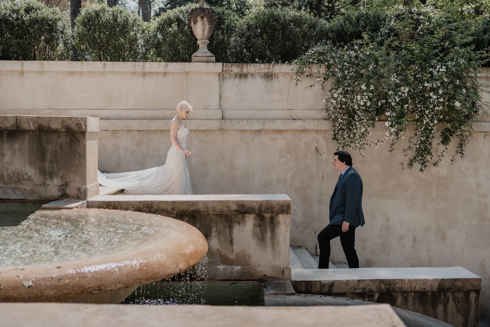 A bride and groom walking hand in hand past a fountain, classic romance framed in timeless architecture