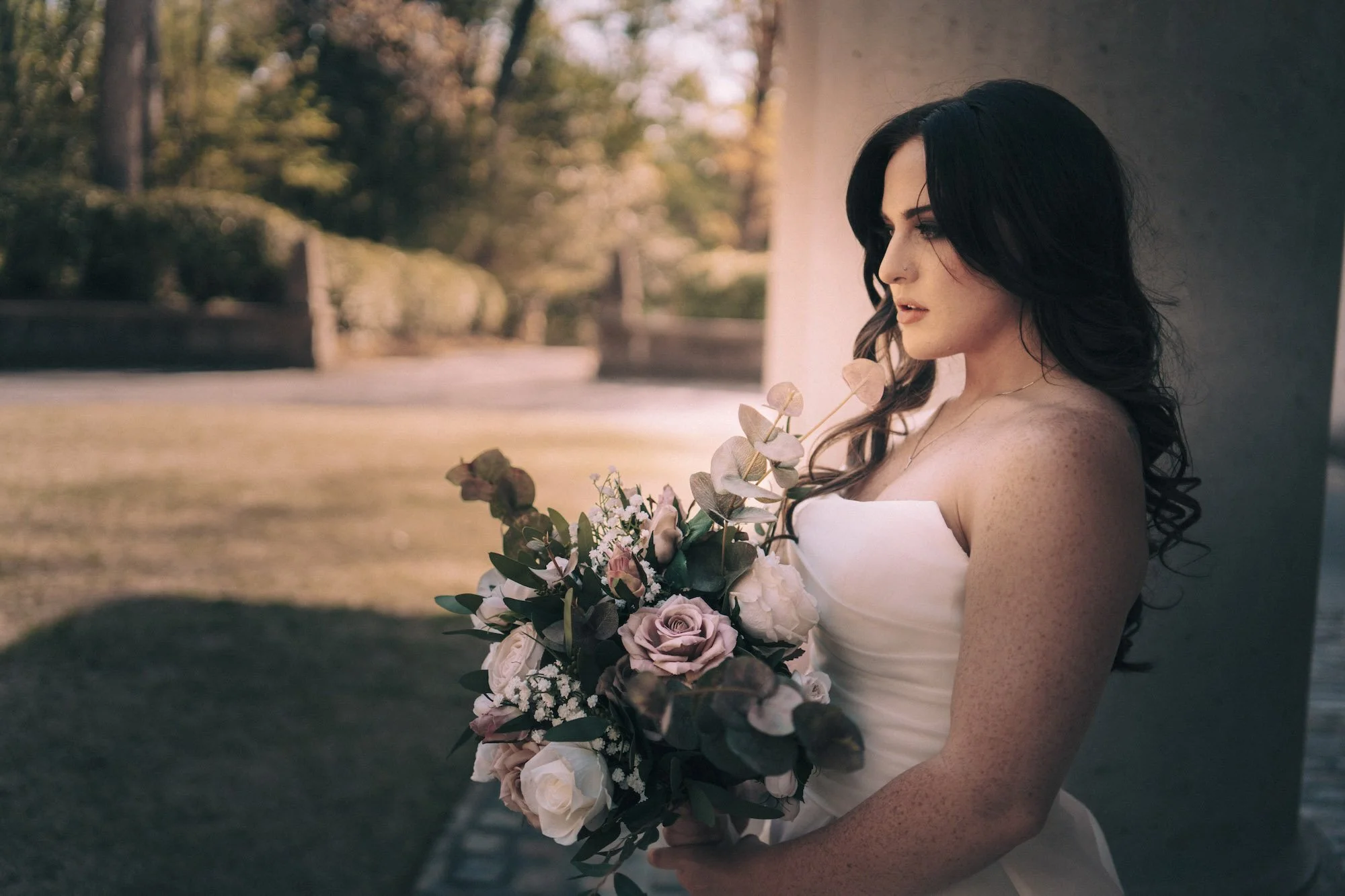 Bride holding a bouquet of roses gazes softly to the side, captured with romantic detail by Caz Isaiah.