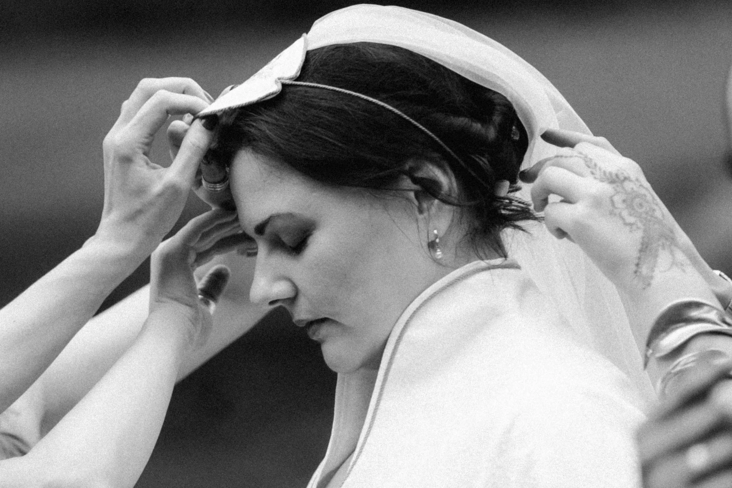 Bride adjusts veil while surrounded by helping hands, quiet portrait inspired by Namibian wedding photography
