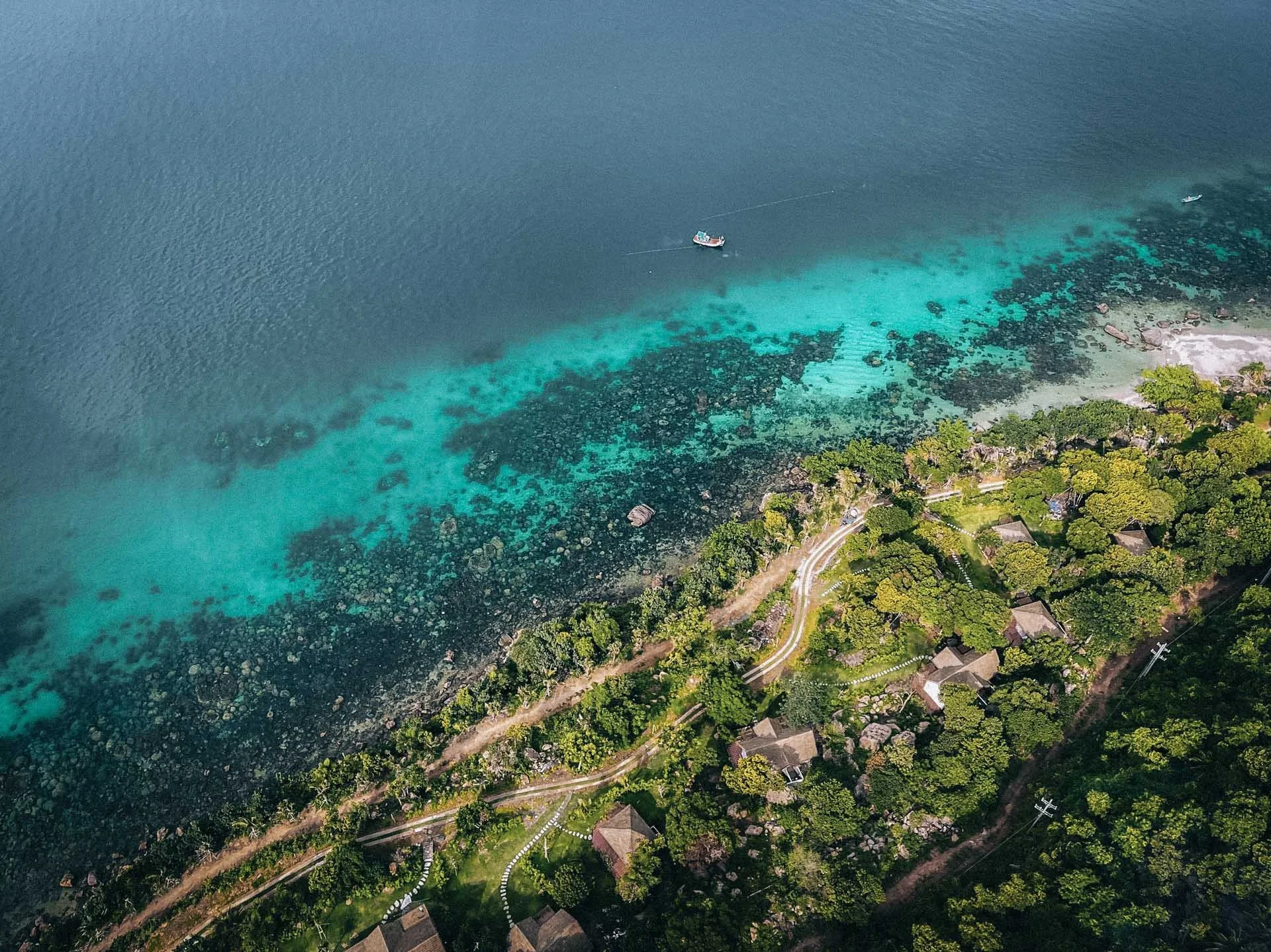 Aerial view of turquoise coastline with lush greenery unfolding into the sea in Vietnam