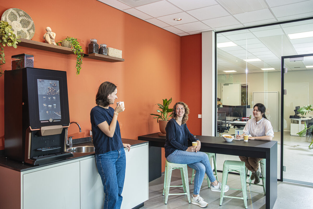 Three people enjoying coffee around a bean-to-cup coffee machine in a modern office break room.