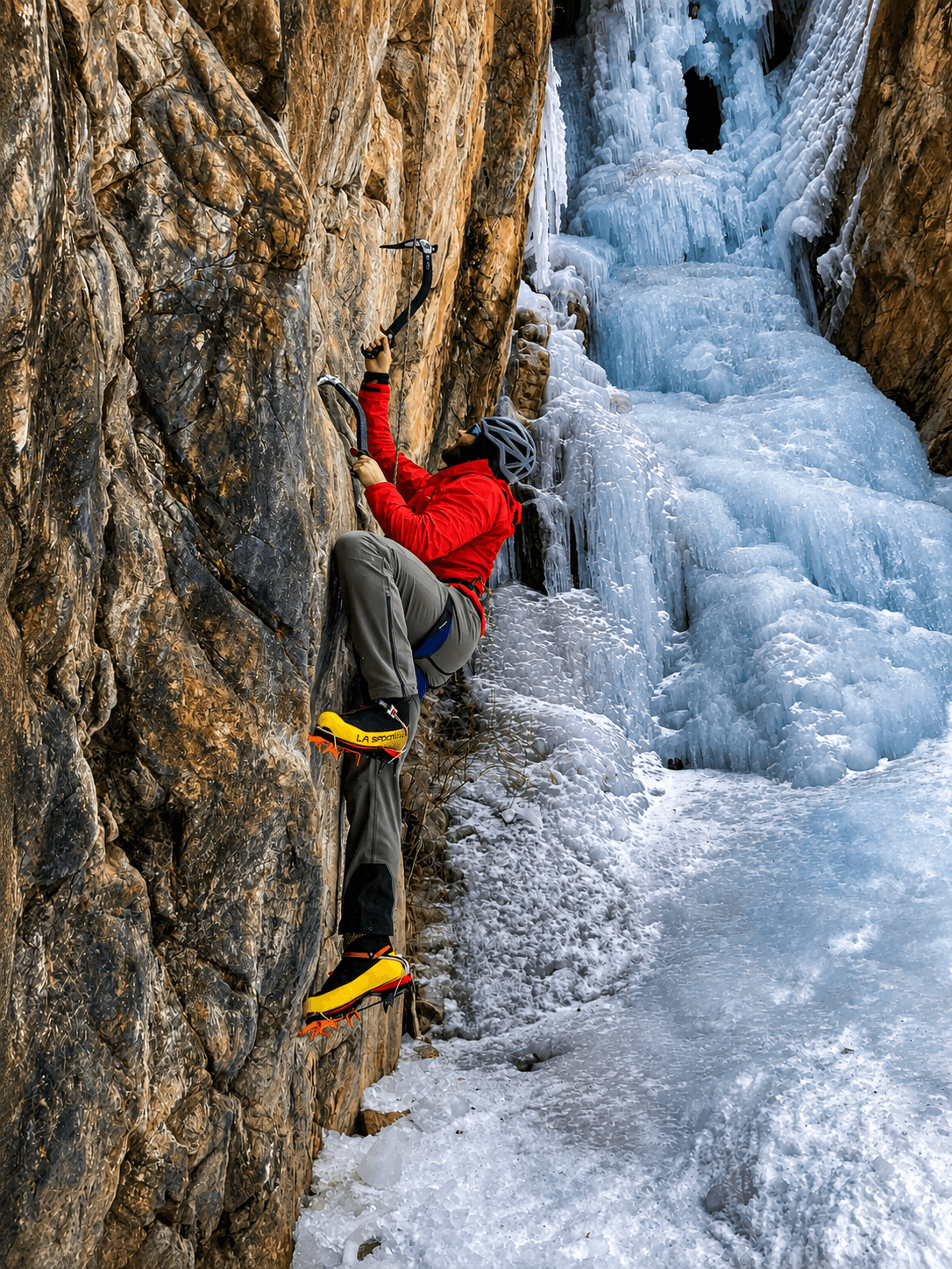 A climber in a red jacket and yellow boots practices mixed climbing on a classic drytooling route in the Ouray Ice Park.