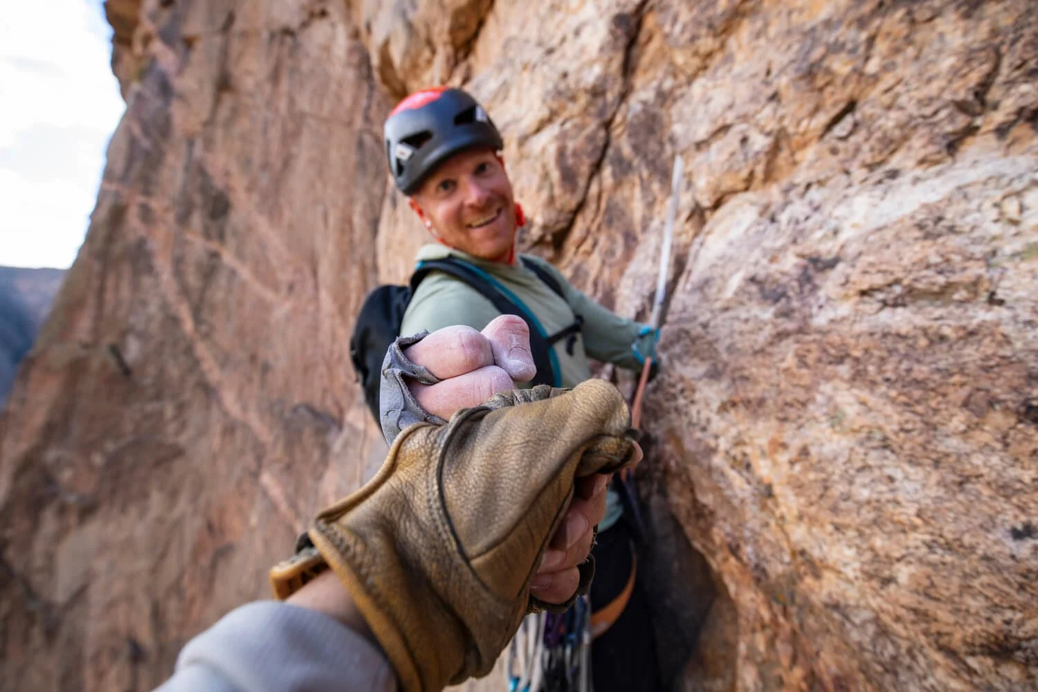 A guide fist bumps a climber wearing belay gloves.