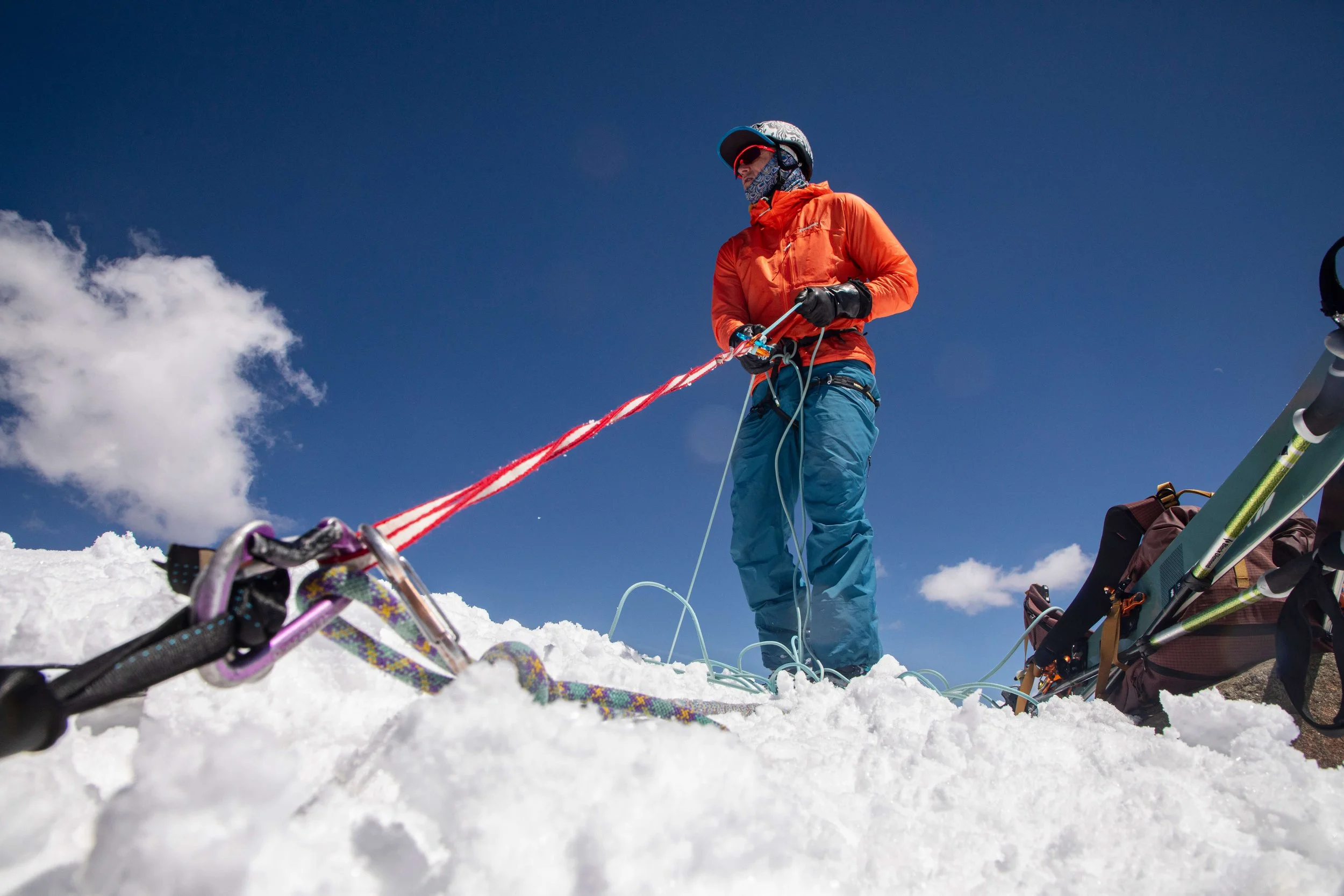 A guide in an orange jacket builds an anchor on the summit of Mount Sneffels.