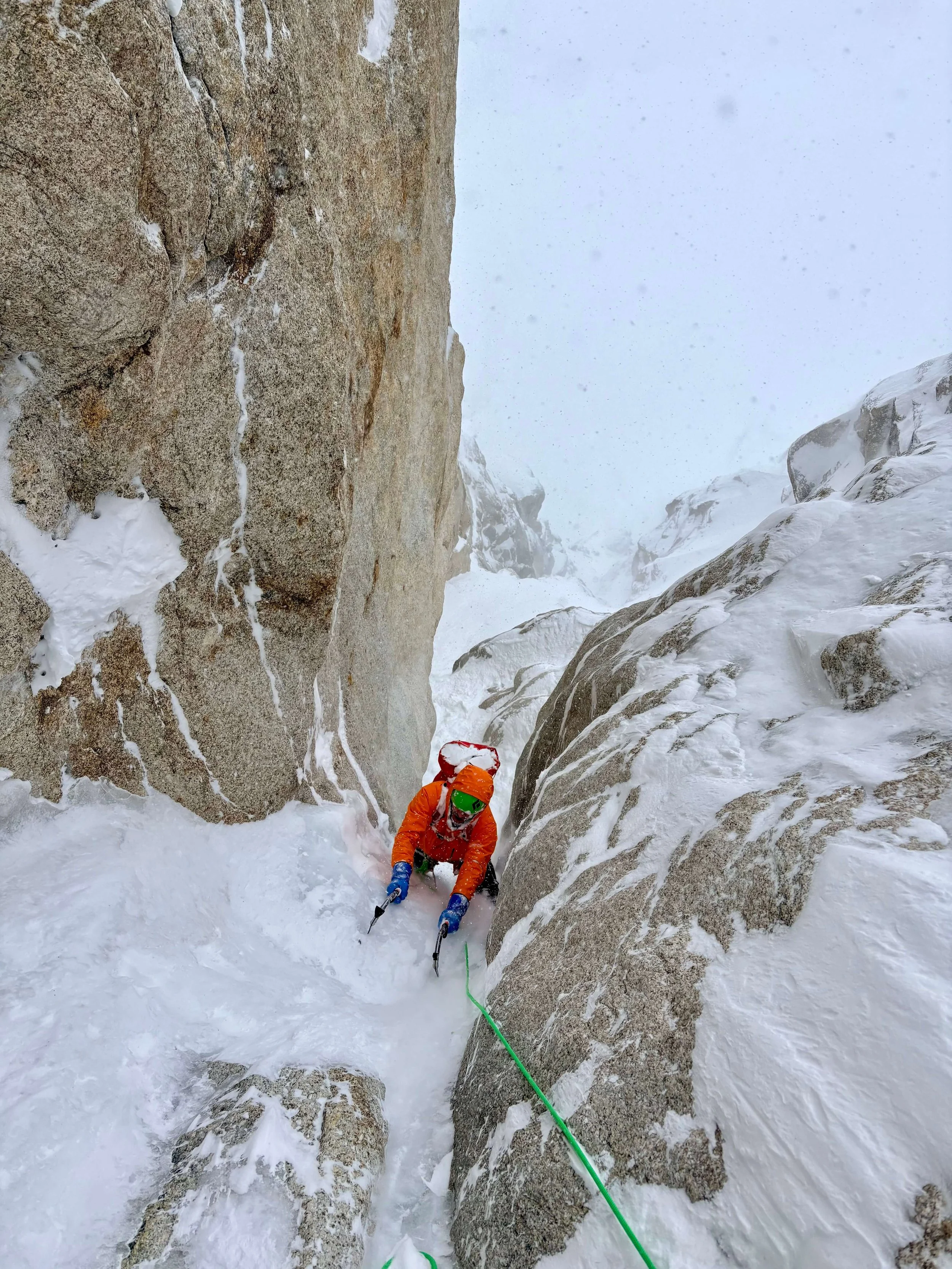 A climber in an orange jacket is climbing the "Narrows" section of the Ham and Eggs route.