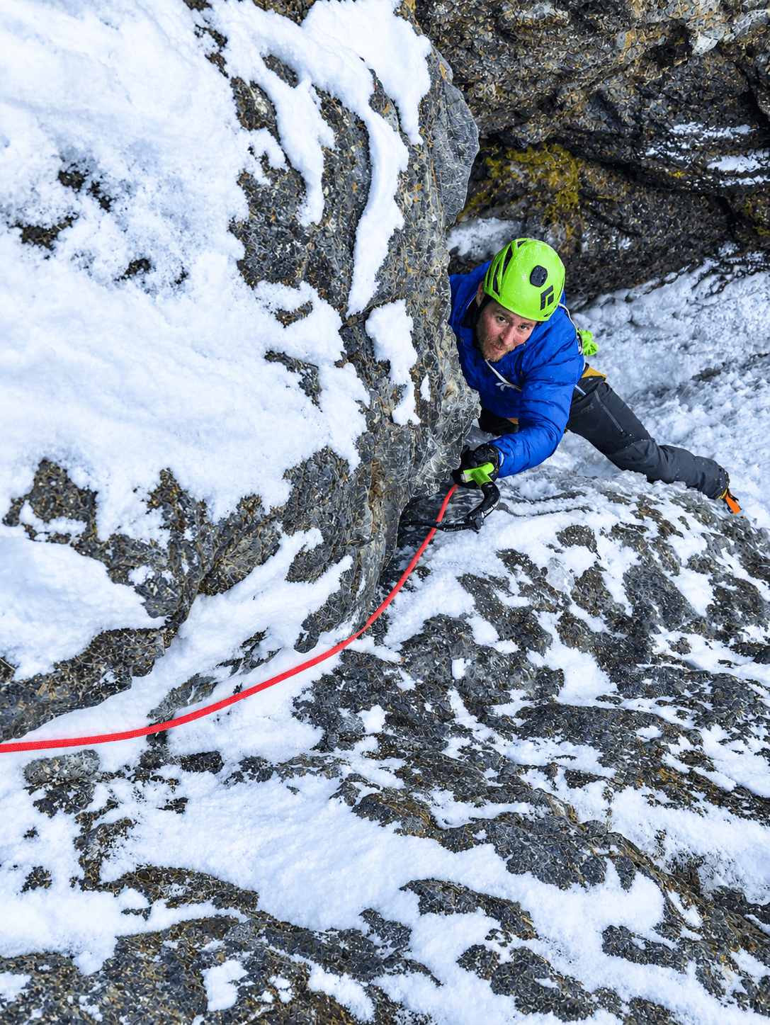 A climber in a blue jacket and green helmet is toproping a mixed climbing route in Ouray, Colorado during an alpine climbing course.