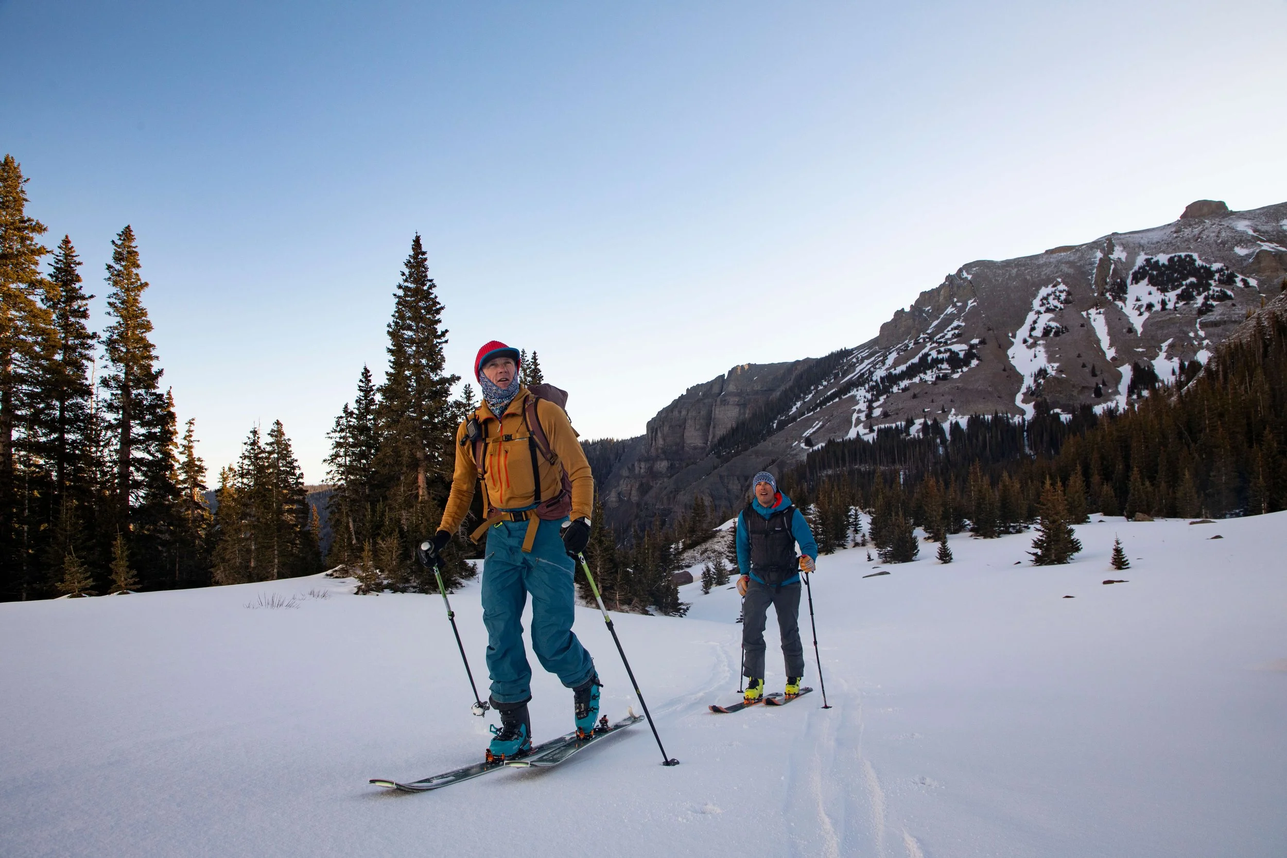 Two skiers traverse below a rocky peak in Colorado at sunrise during a ski mountaineering course.