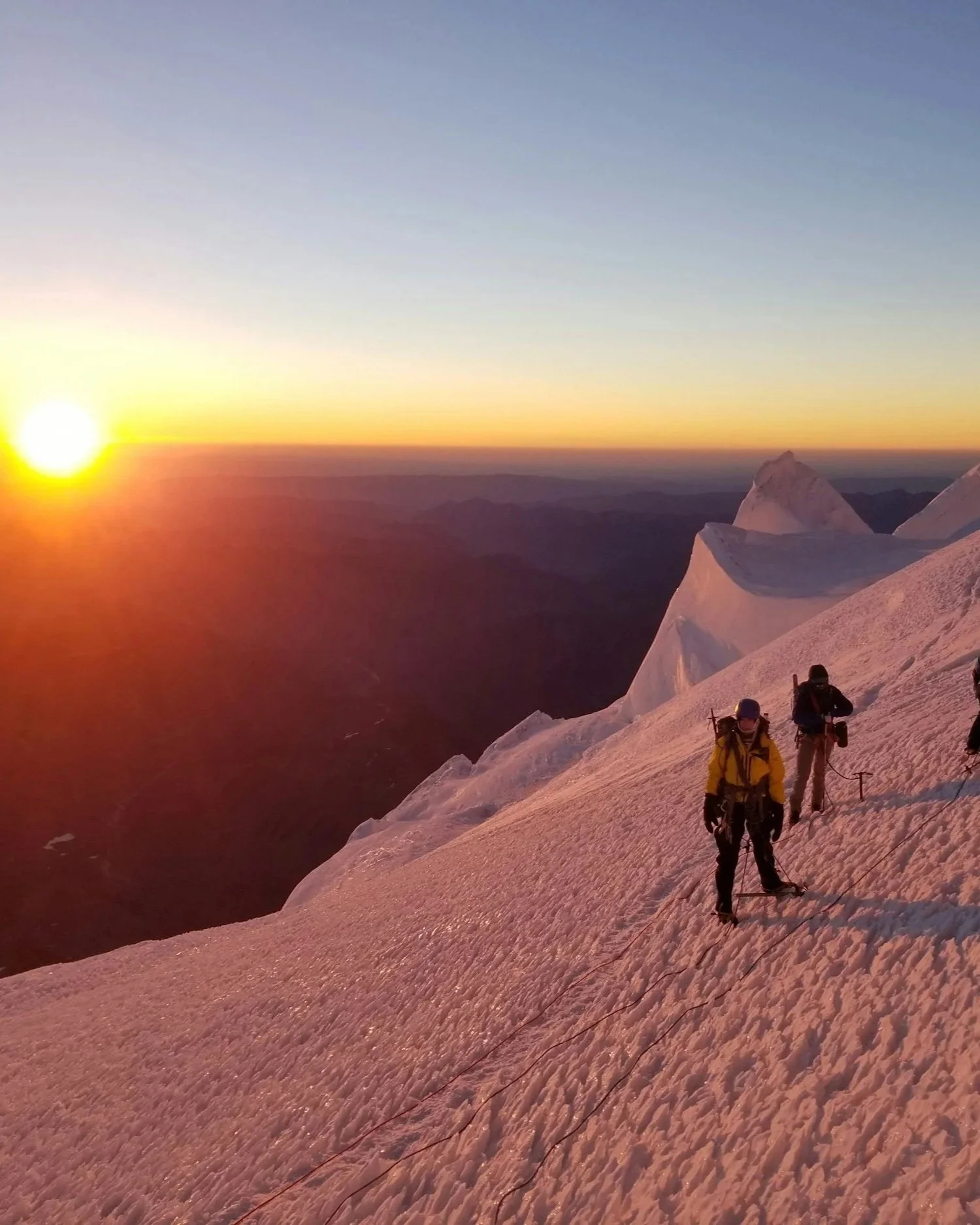 Climbing up the glacier on Mount Rainier with the sun rising in the background.