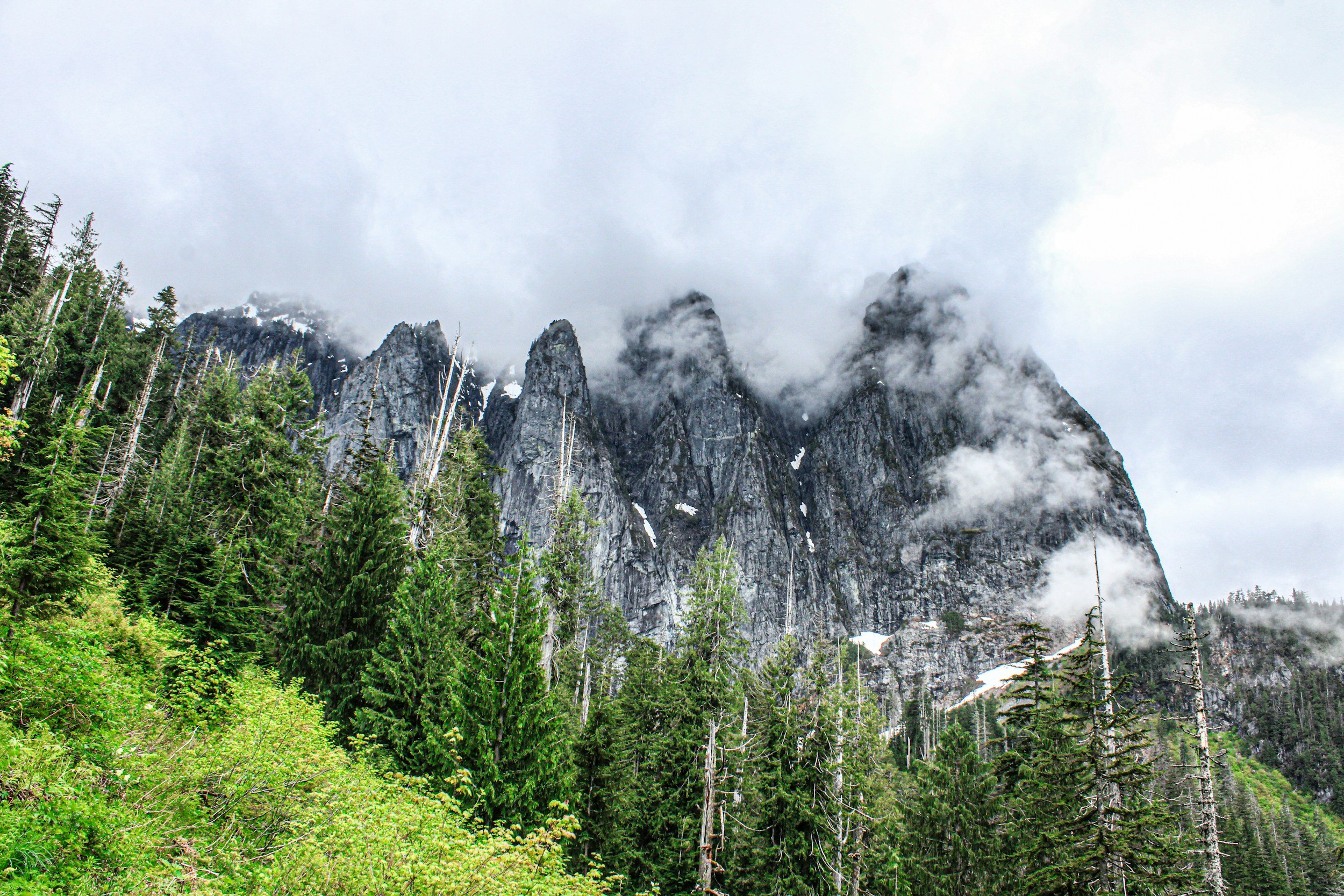Granite peaks above Index, Washington rise into stormy clouds with a lush green forest below.