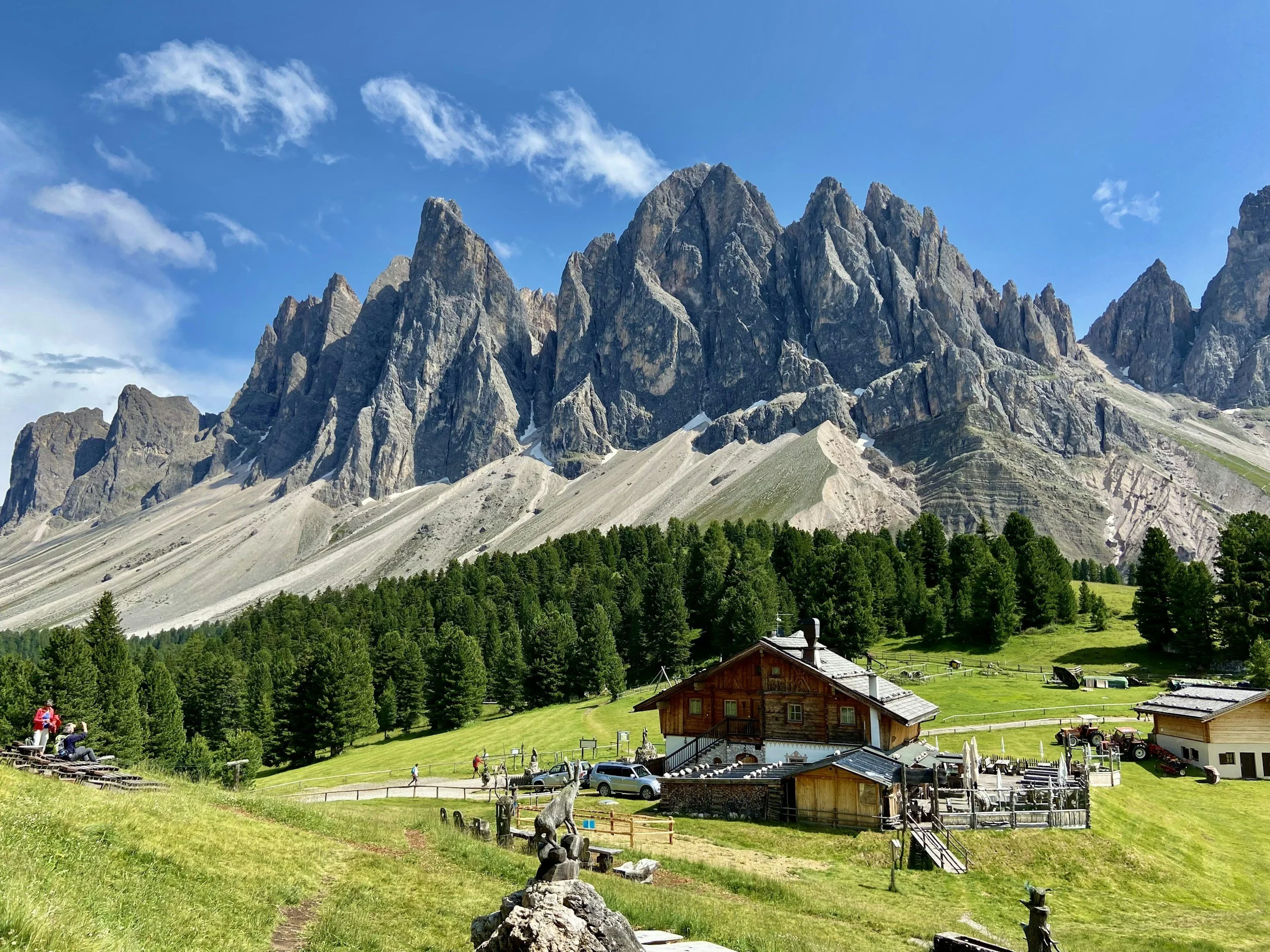 Limestone cliffs at the Dolomites rise above a rustic cottage at the base.