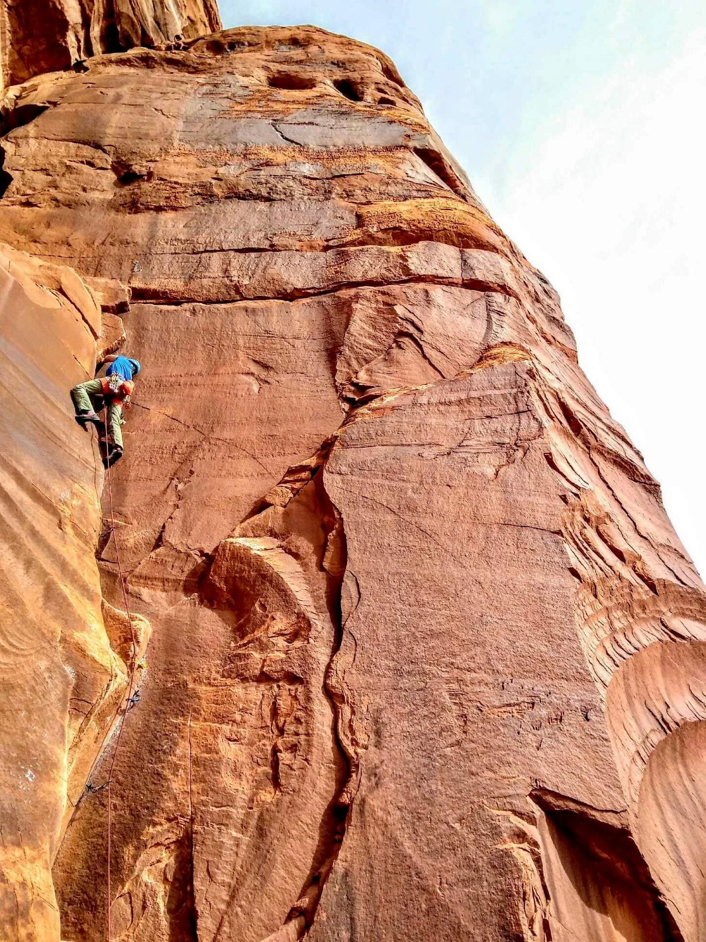 A climber in a blue shirt is leading a crack climb in Escalante Canyon.