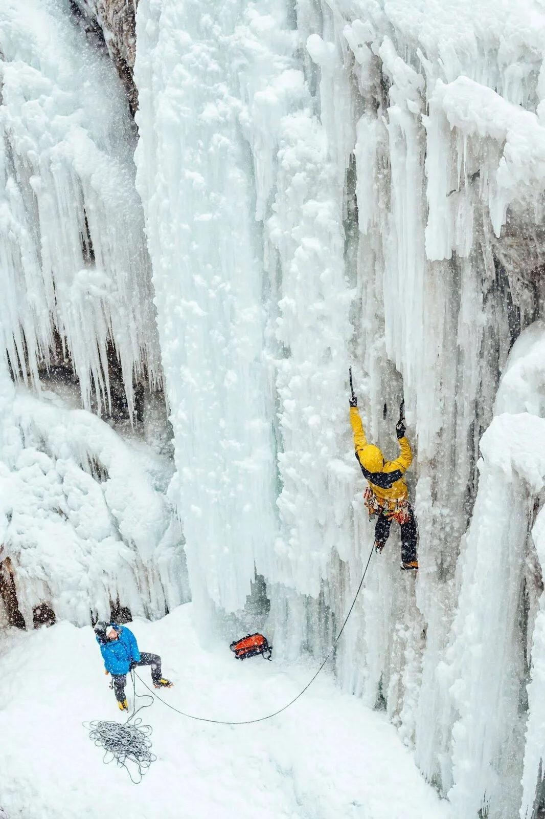 A guide in a yellow jacket is leading a pitch of ice in the Ouray Ice Park with a belayer in a blue jacket below.