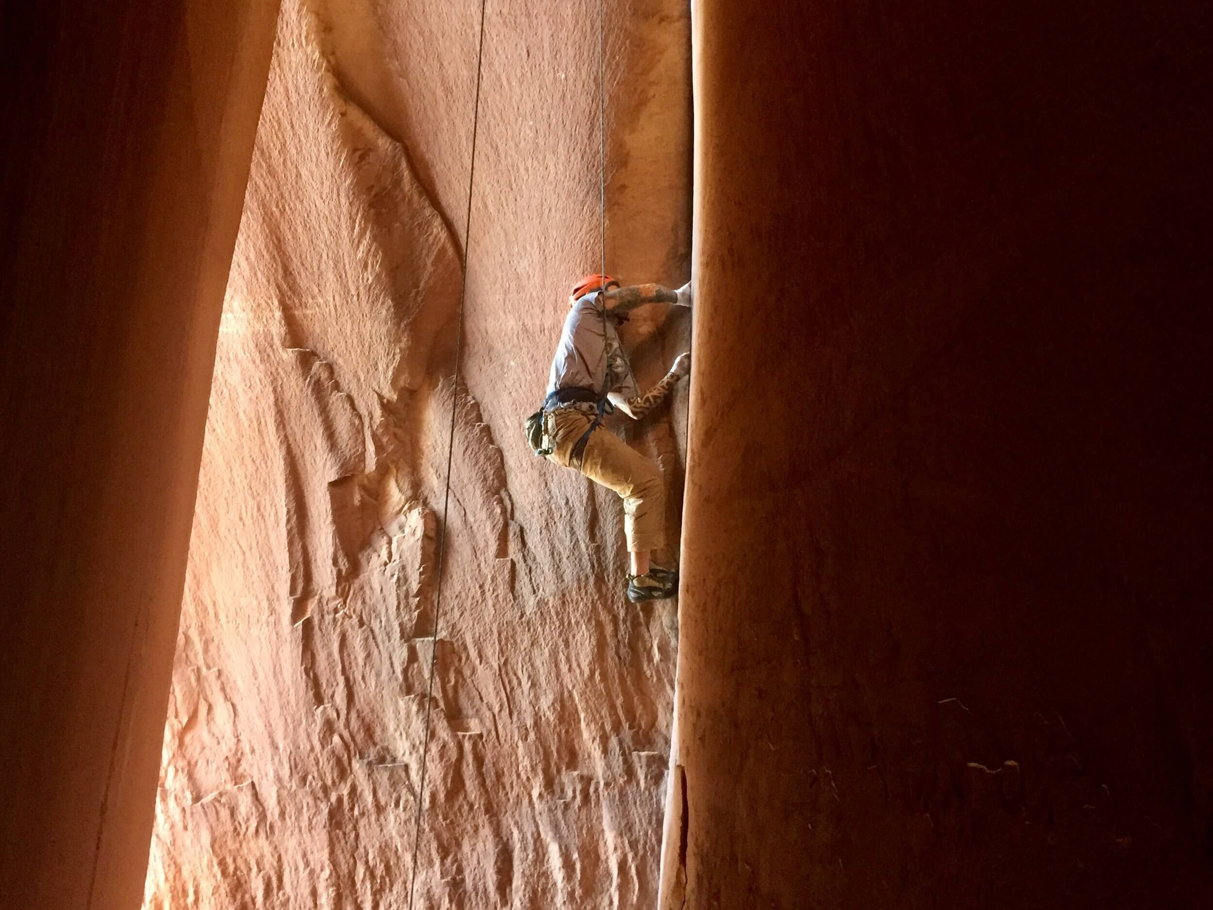A person crack climbing up a narrow canyon with red sandstone cliffs.