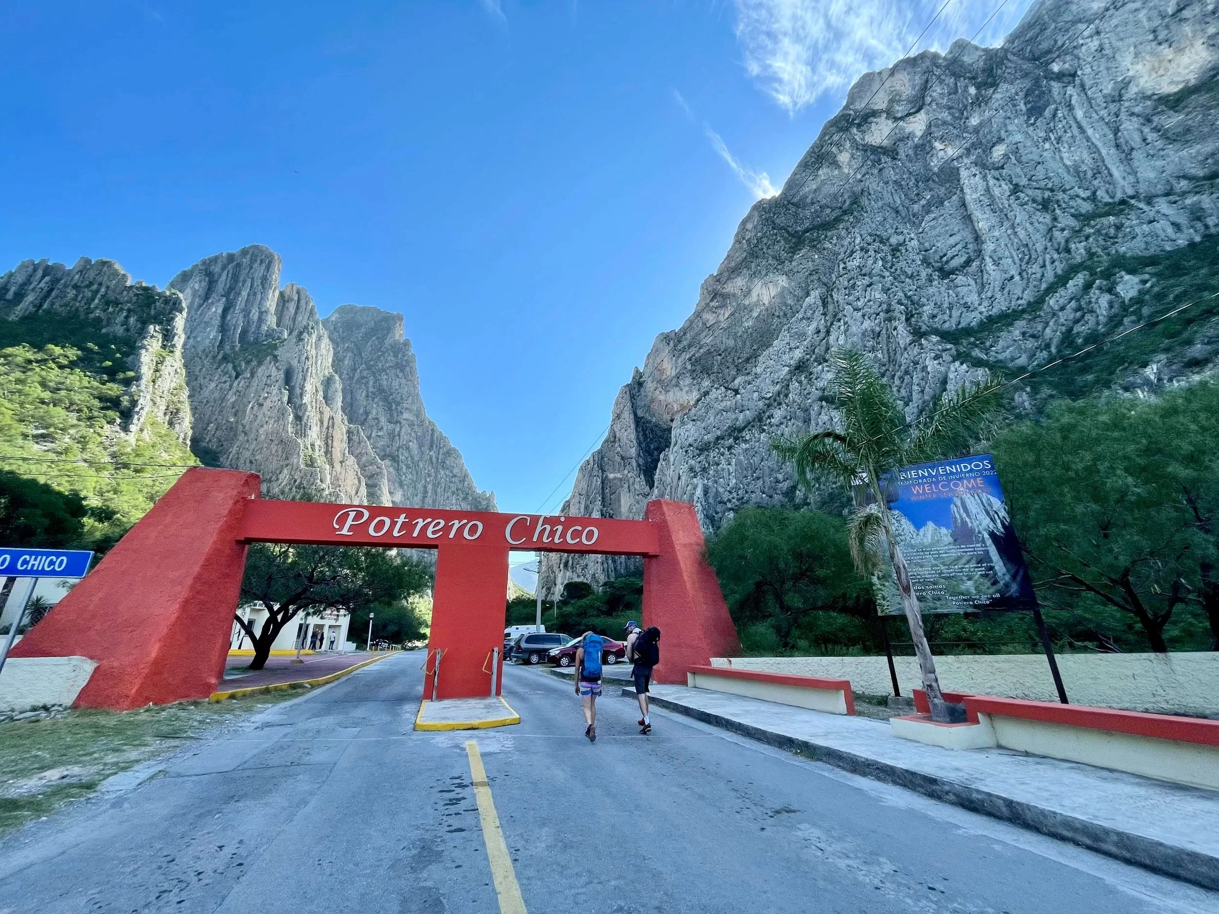 Two climbers walk through the entryway arch at El Potrero Chico with limestone cliffs rising in the background.