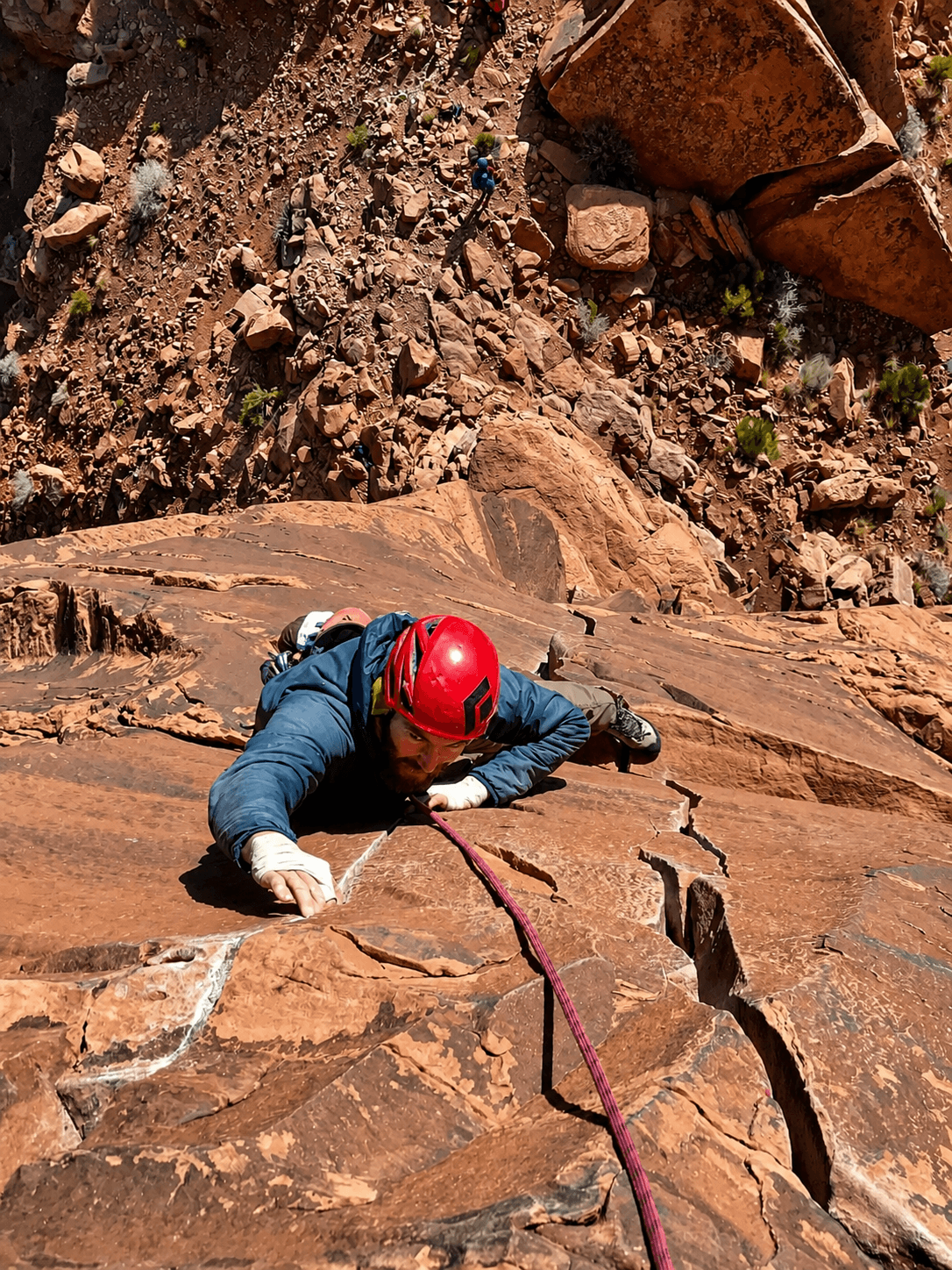 A climber in a red helmet is jamming his fingers in a crack on the route, Fine Jade on The Rectory in Castle Valley.