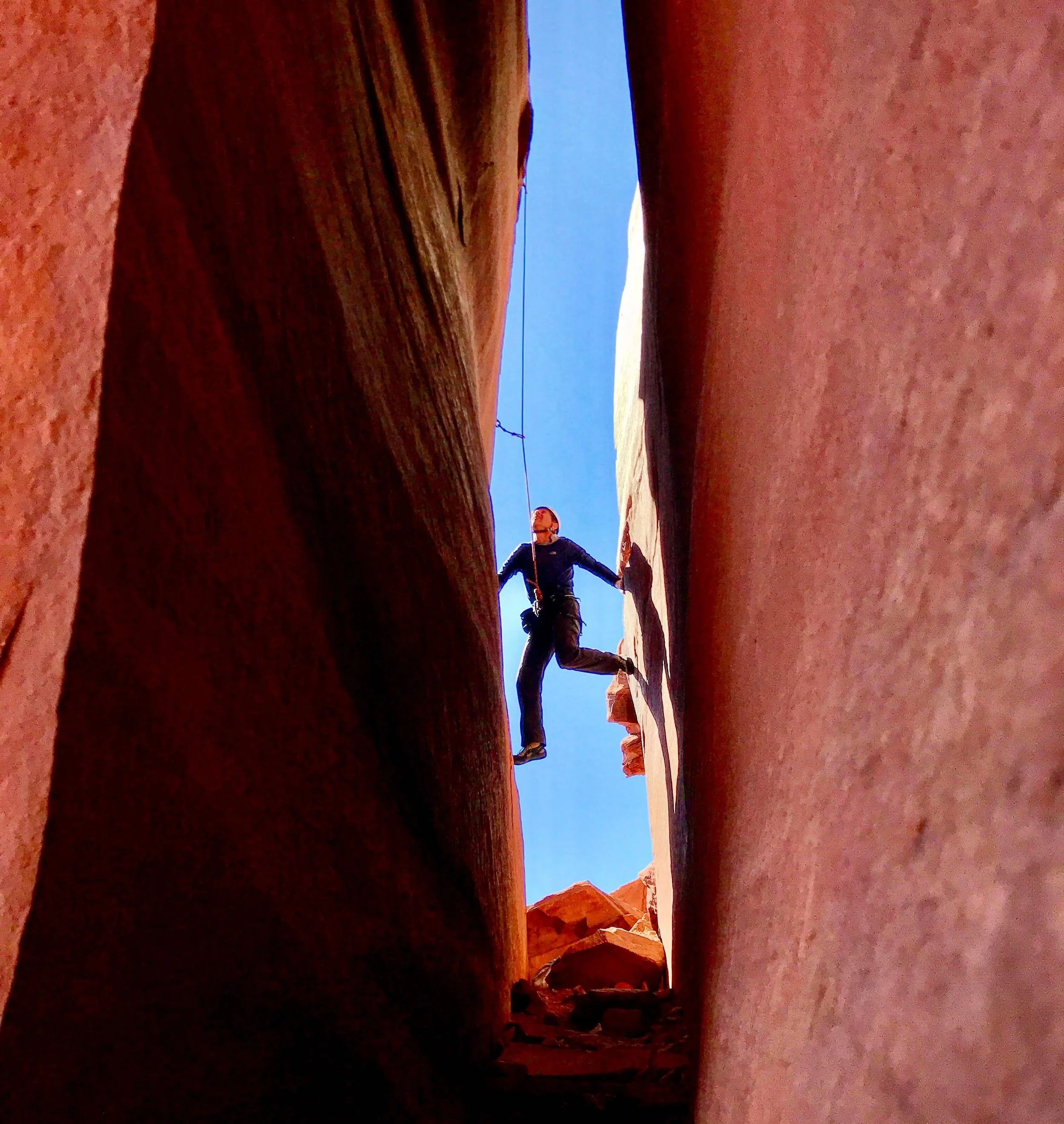 A climber using chimney technique to climb an offwidth crack during a crack climbing course in Escalante Canyon.
