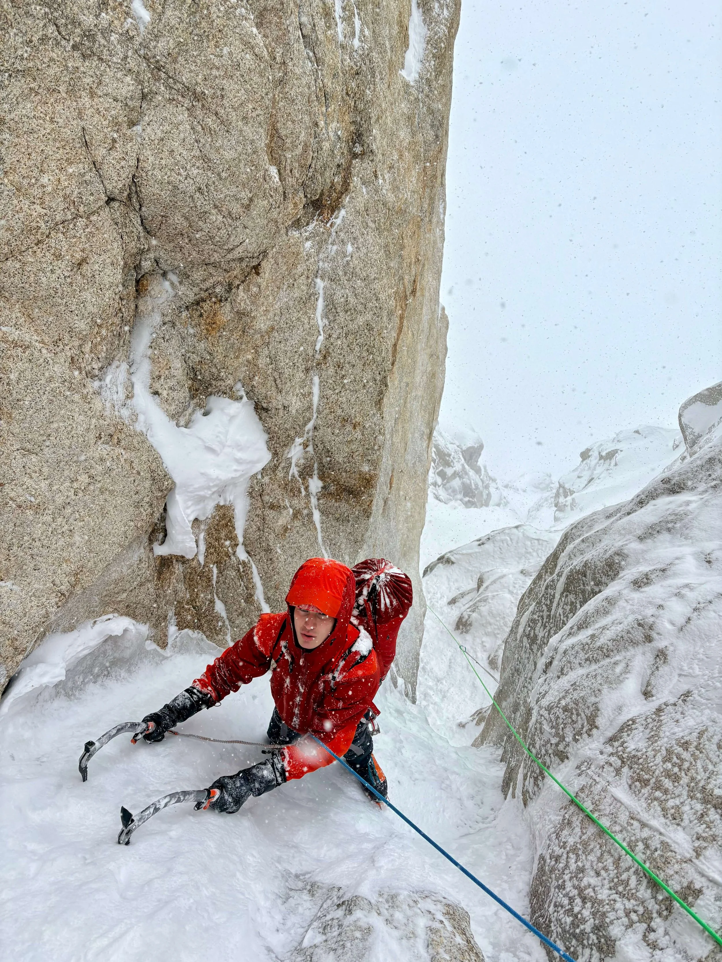 An alpinist in a red jacket is climbing up a snowy couloir on the route Ham And Eggs on the Moose's Tooth in Alaska.