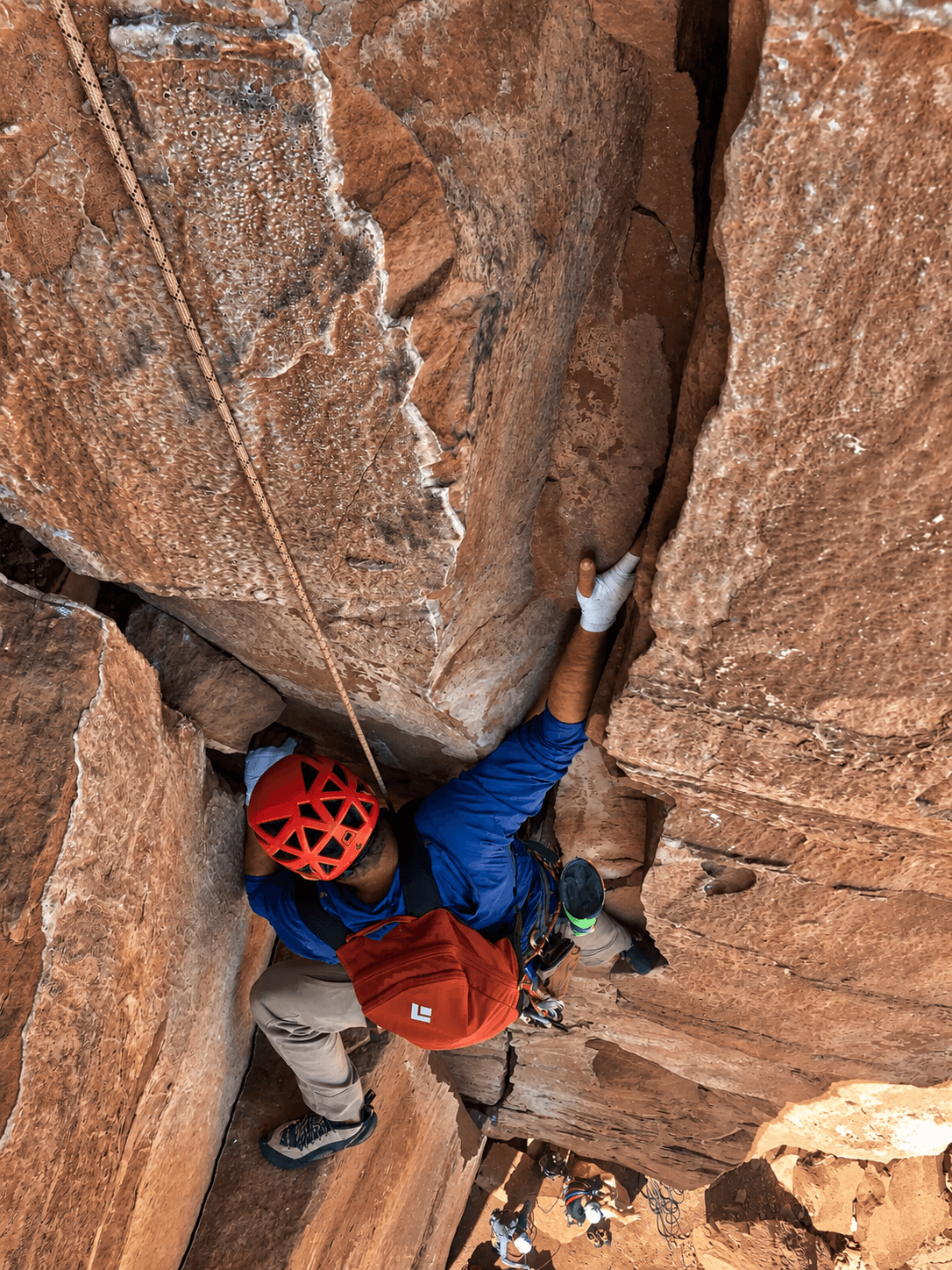 A climber in a red helmet is hand jamming a crack on Castleton Tower's North Chimney route.