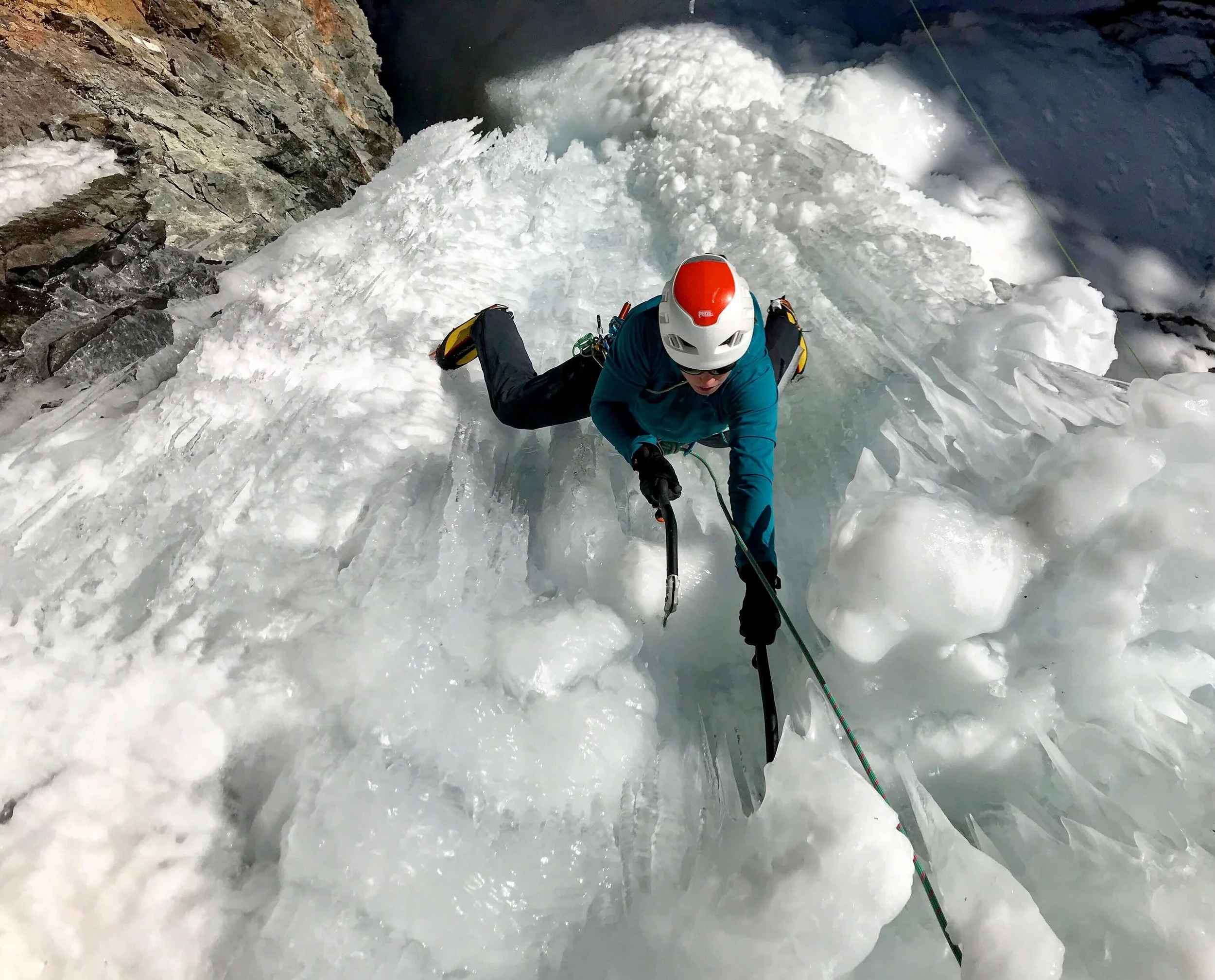 An ice climber in a blue jacket and orange and white helmet is swinging her ice tool into a steep pillar in Eureka, Colorado.