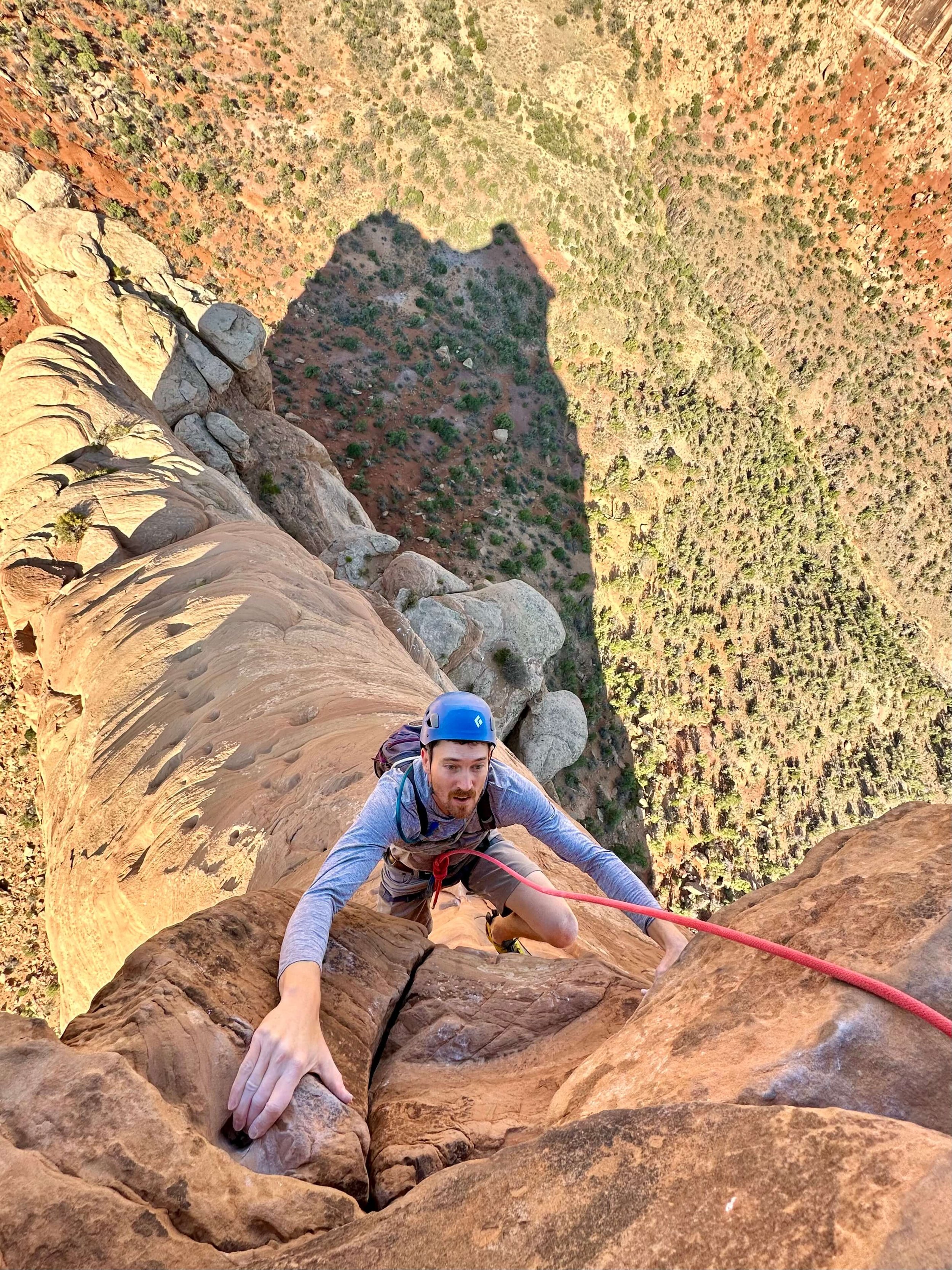 A climber in a blue helmet with a pink rope is climbing the steep headwall on Otto's Route in Colorado National Monument.