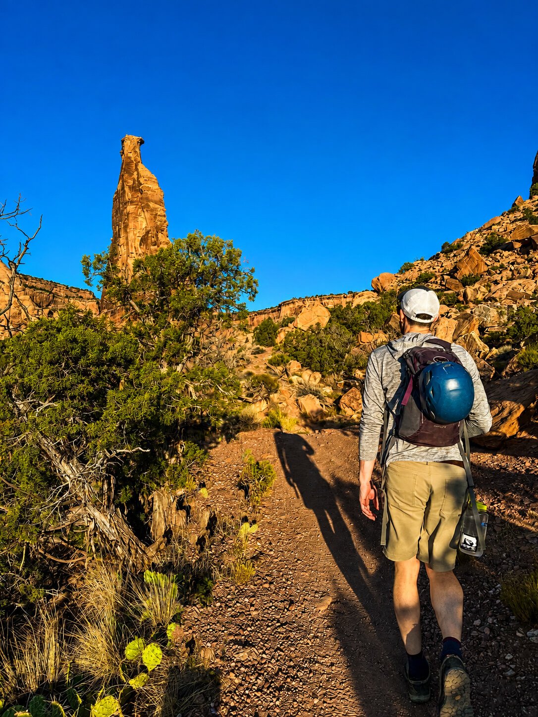 A climber hikes in Colorado National Monument with Independence Monument in the background.
