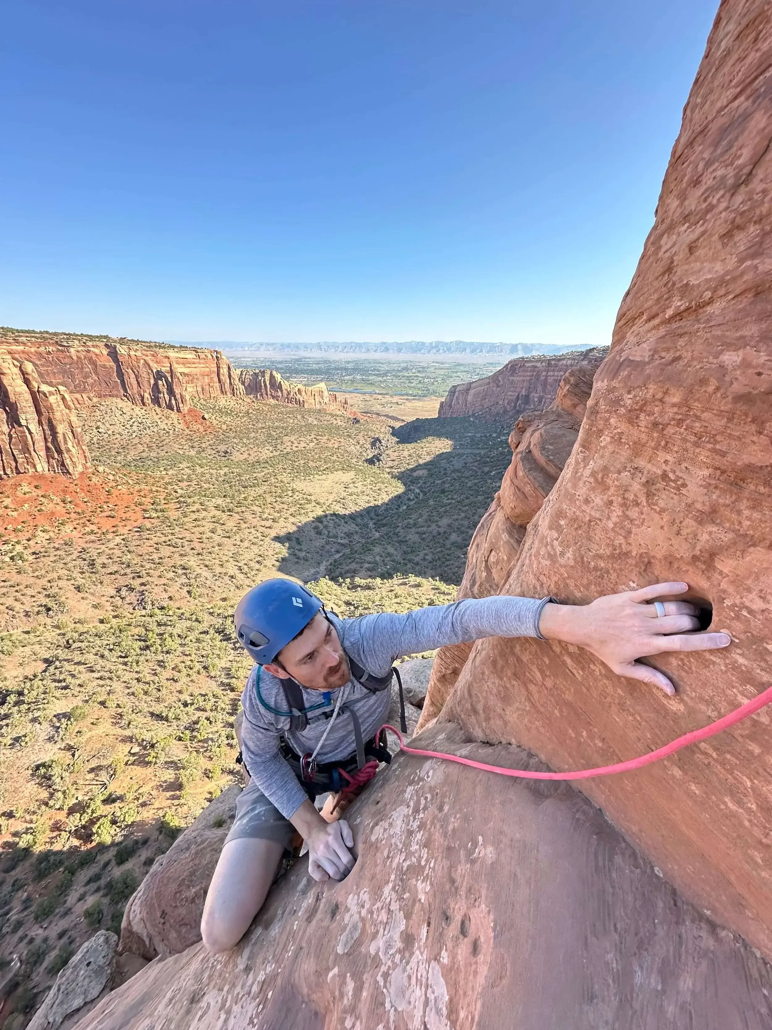 A rock climber in a blue helmet is reaching into a pocket on Independence Monument in Colorado National Monument.