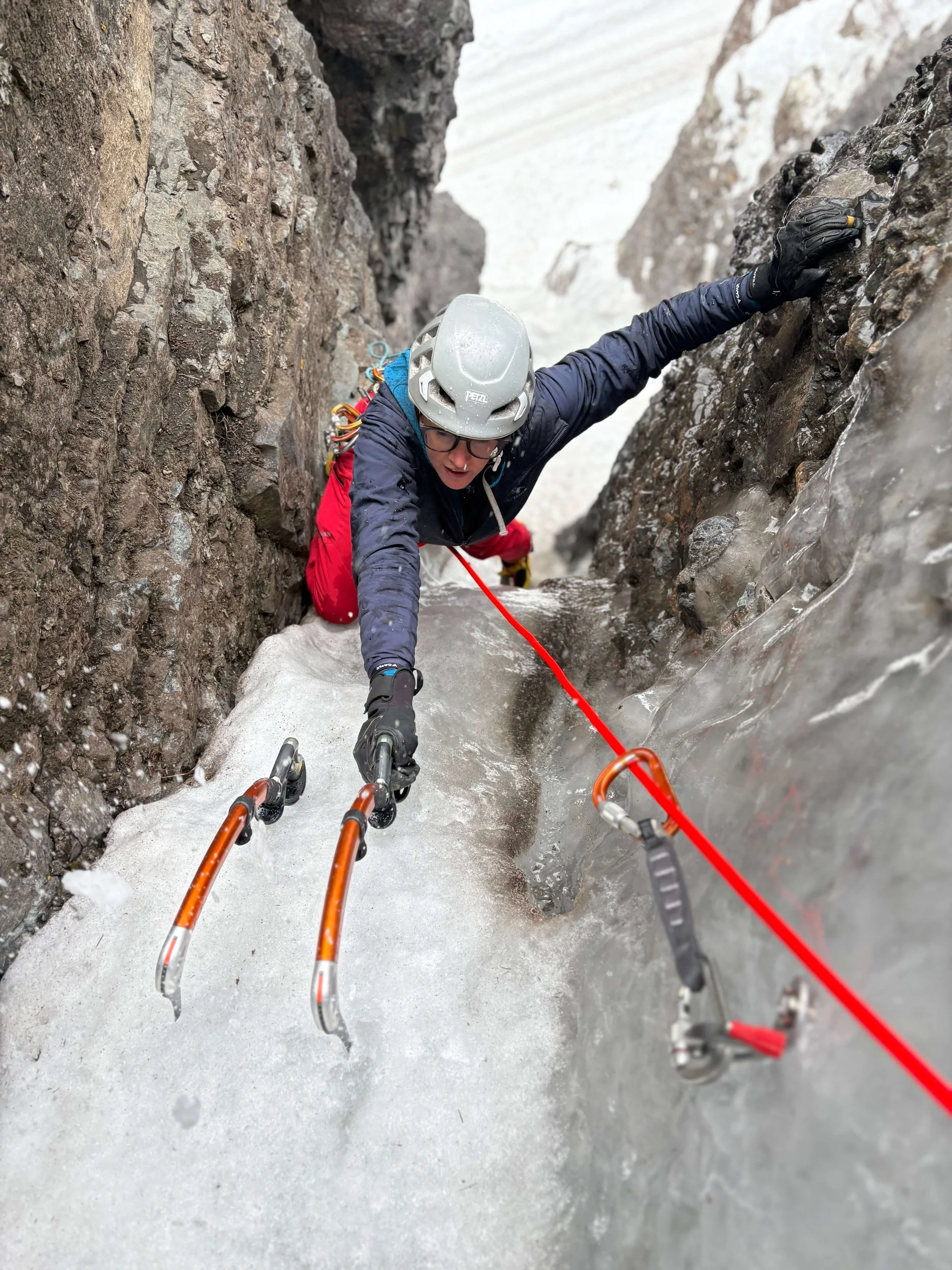 A climber swings her ice tools into the ice in a narrow chimney.