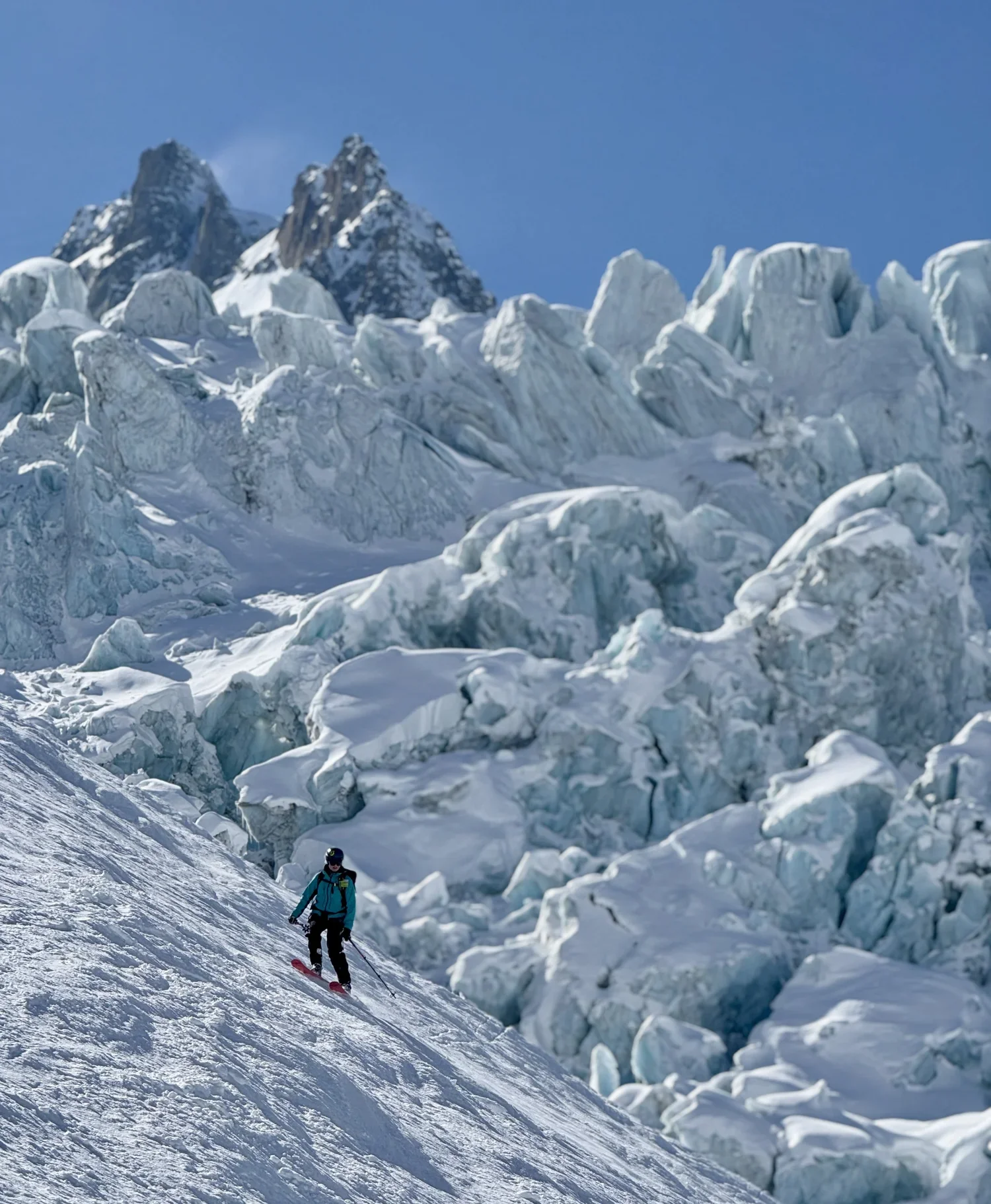 A skier descends a steep slope on the Haute Route with icy seracs and jagged peaks in the background.