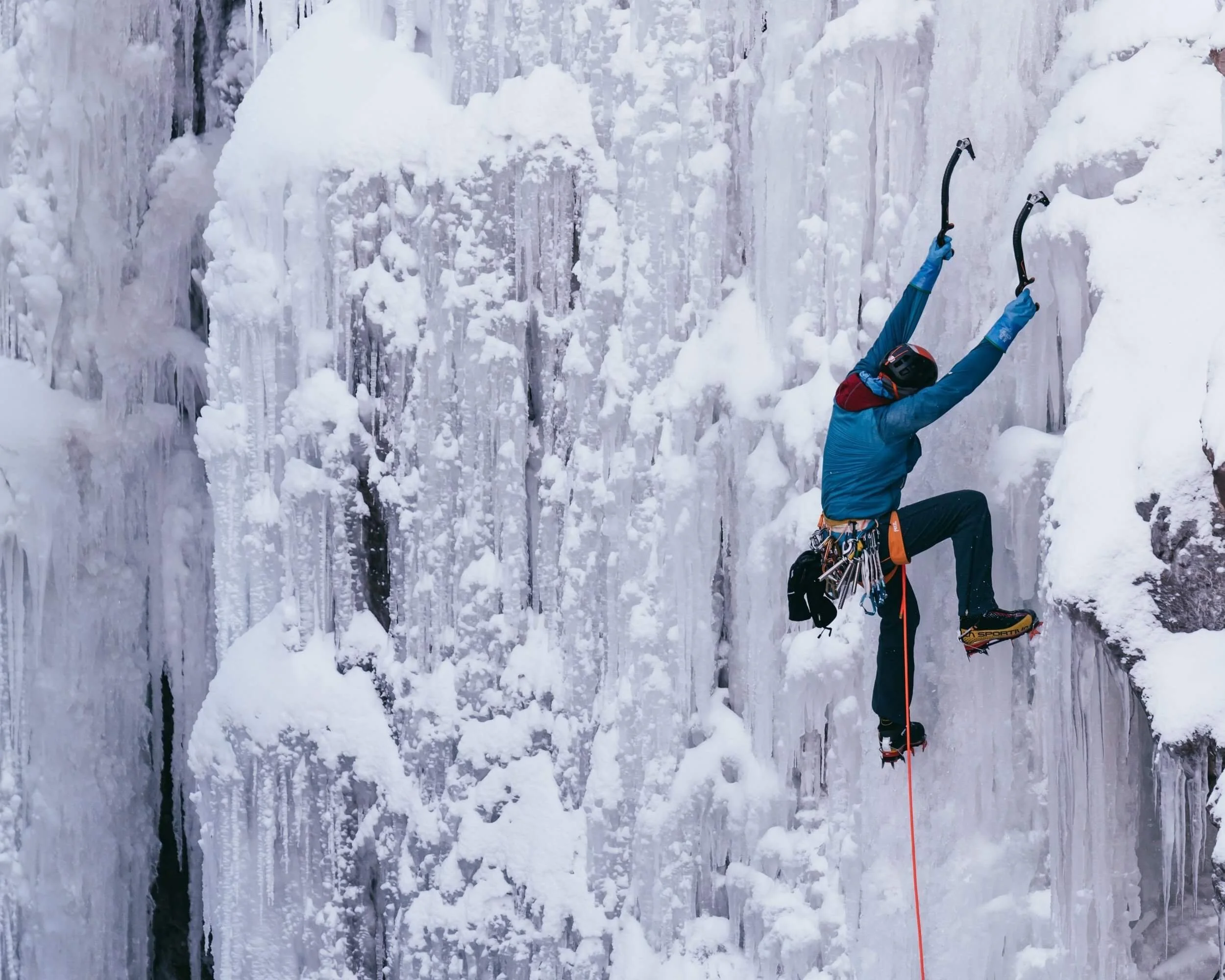 A person in a blue jacket is lead ice climbing on a steep route in the Ouray Ice Park.