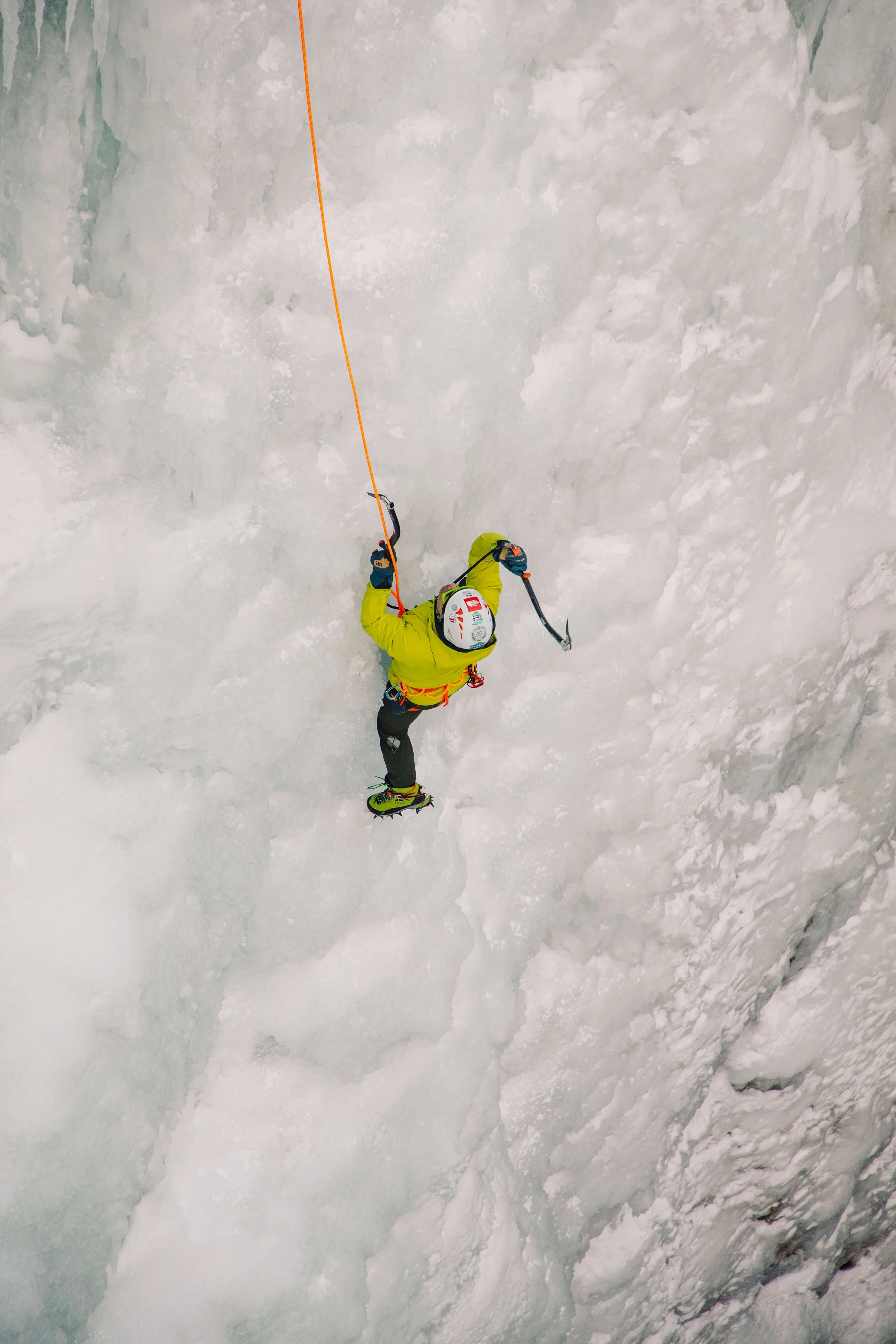 An ice climber in a yellow jacket is swinging his ice tool on a steep pitch in the Ouray Ice Park during an ice climbing course.