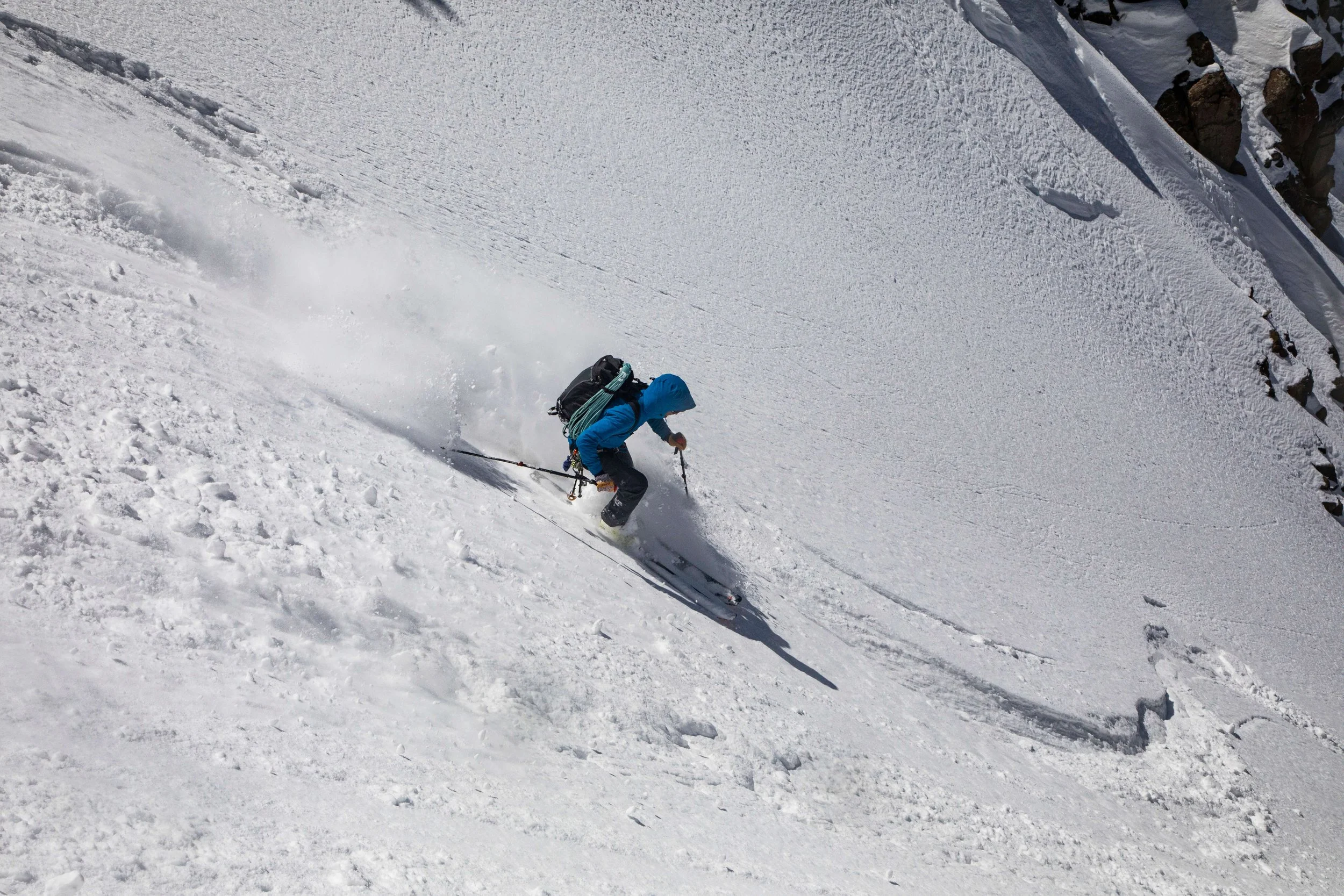 A skier in a blue jacket is carving on a steep face and spraying powder snow while descending the Snake Couloir on Mount Sneffels.