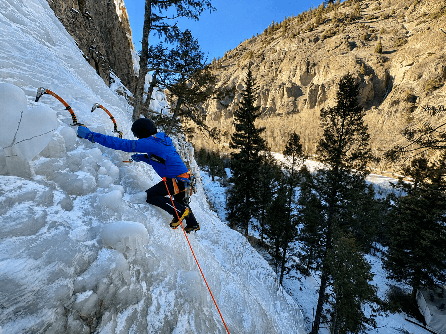 A climber is learning how to lead at the Lake City Ice Park. He is placing an ice screw while being belayed by his partner below.