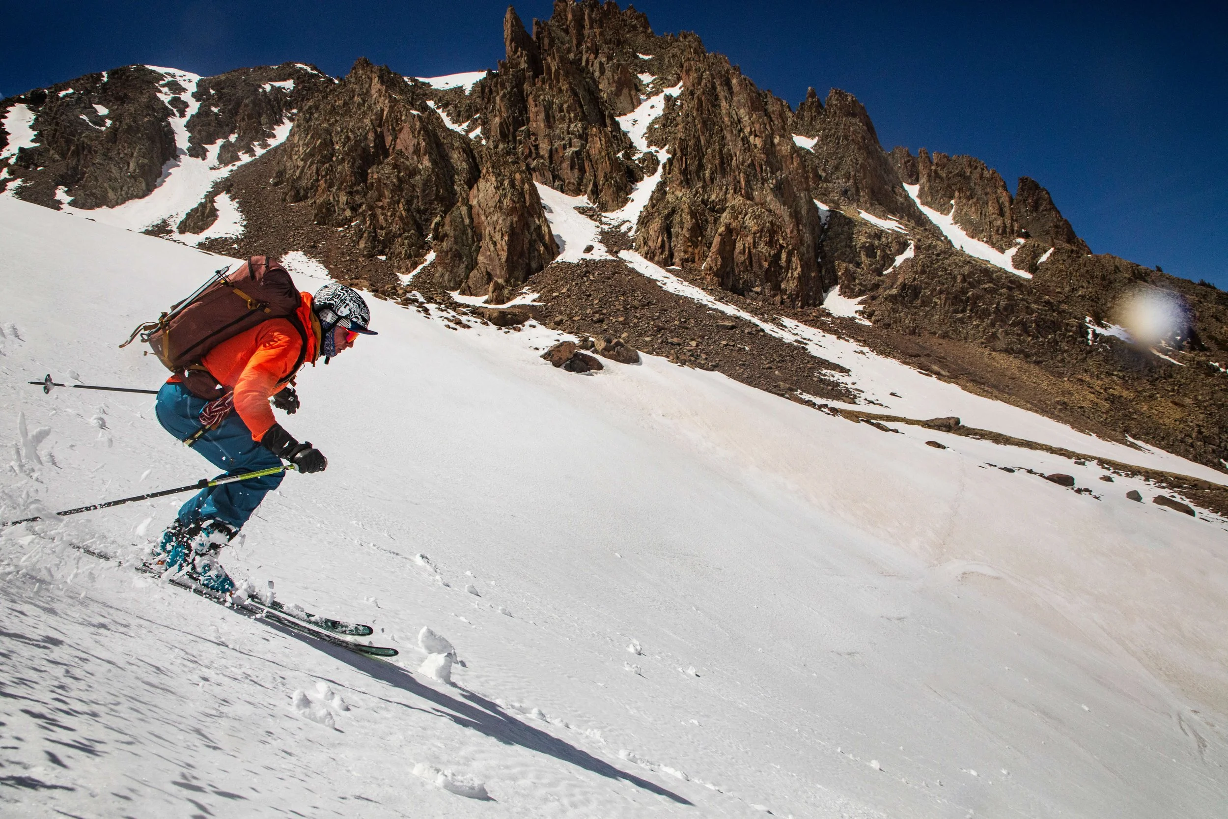 A skier in an orange jacket and blue pants is skiing spring corn in the San Juan Mountains.