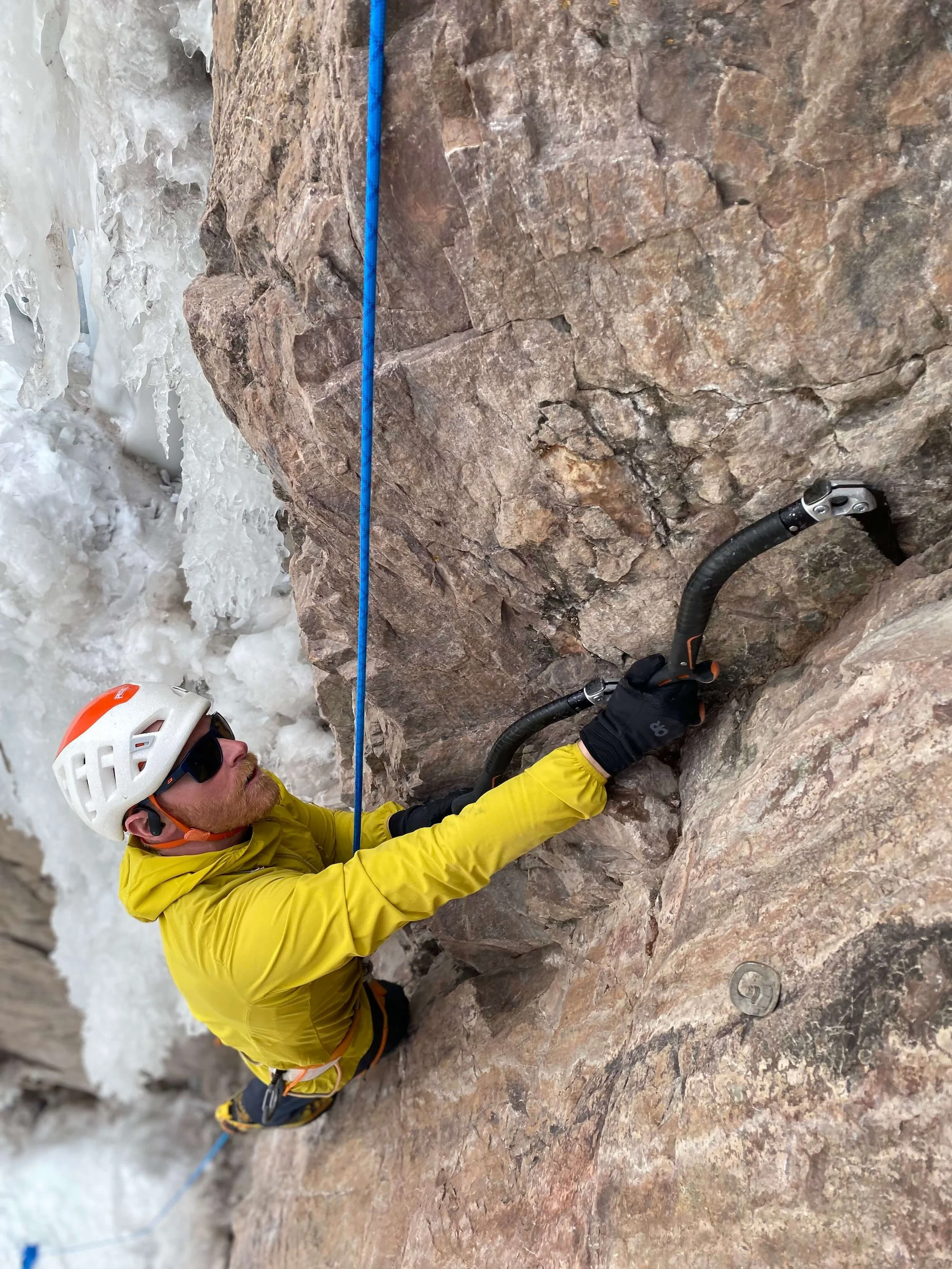 A guide wearing a yellow jacket is dry tooling a route in the Ouray Ice Park during a Mixed Climbing course.
