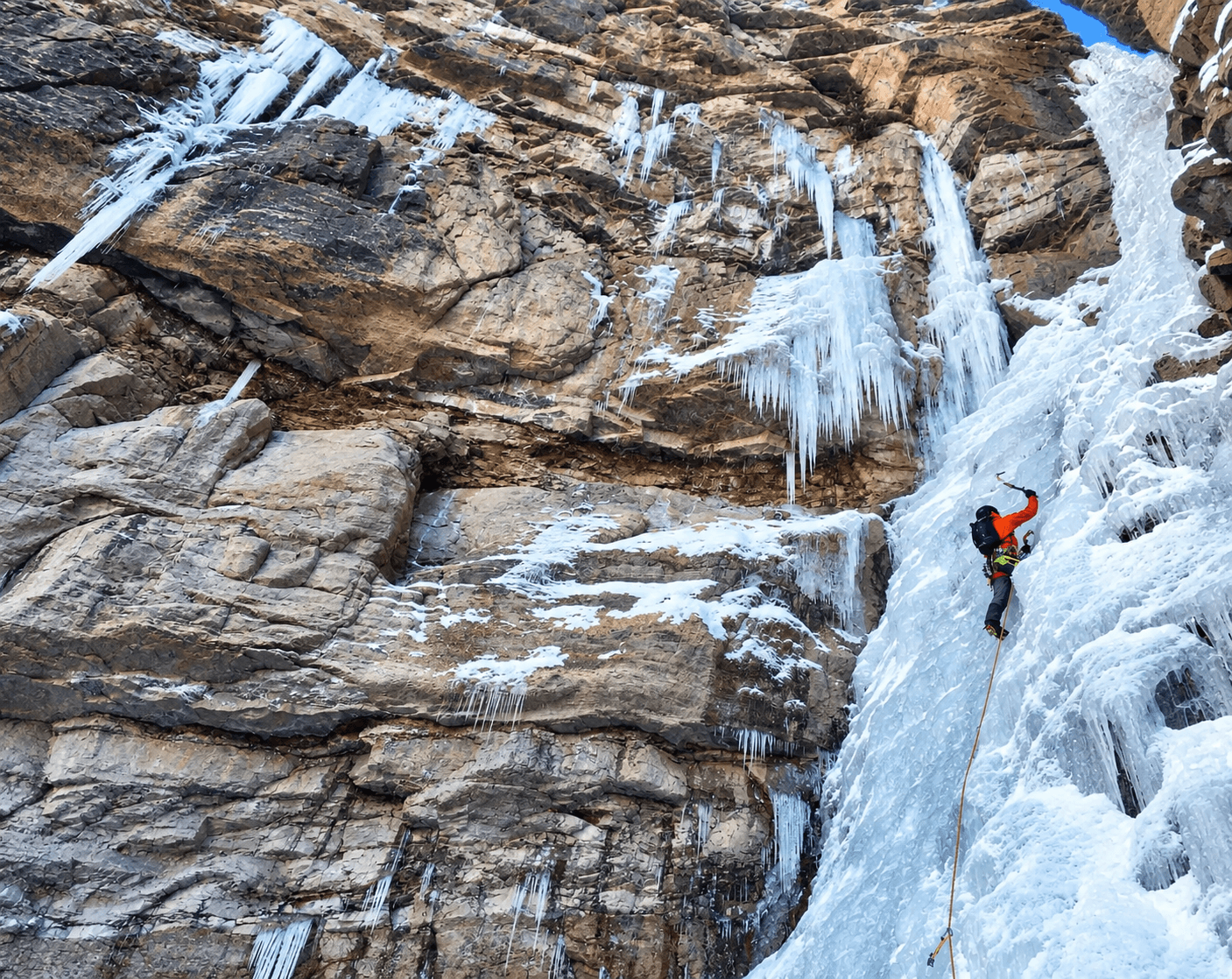 An ice climber leads a backcountry multipitch route in Ouray with red rock and blue ice. 