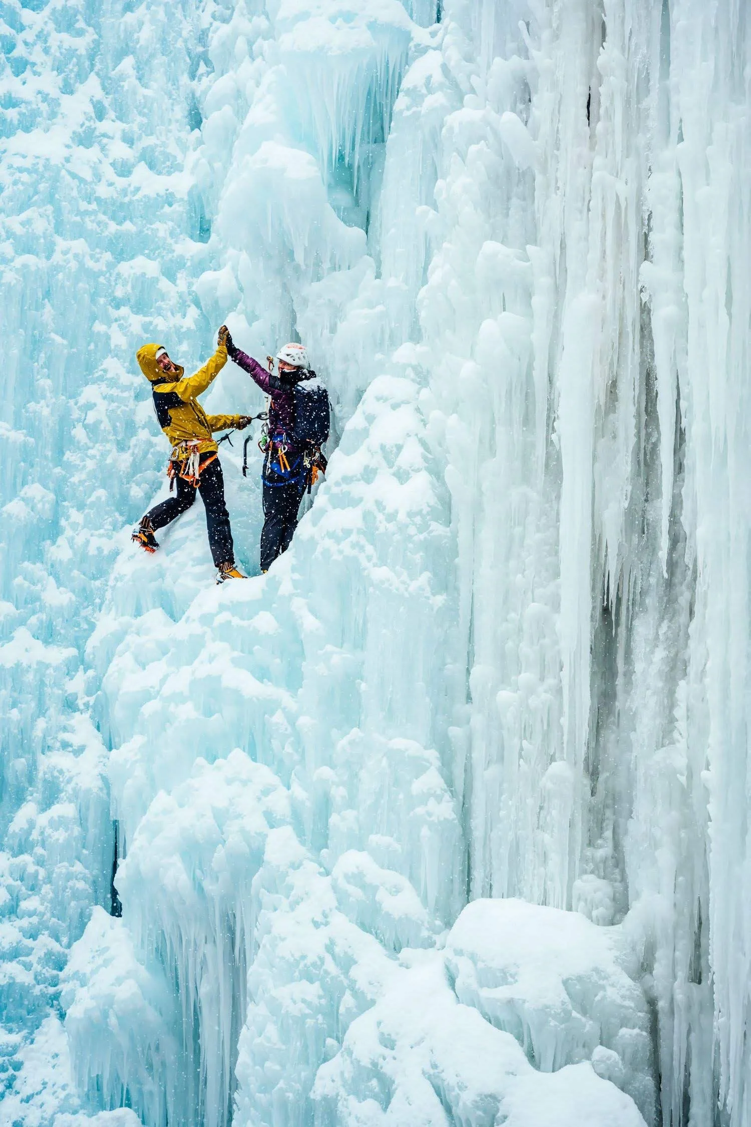 Two ice climbers high five midway up a lead climbing route in the Ouray Ice Park.