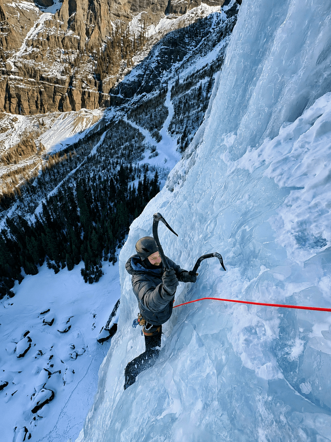 A climber follows a steep pitch on Bridal Veil Falls with Ajax Peak in the background.